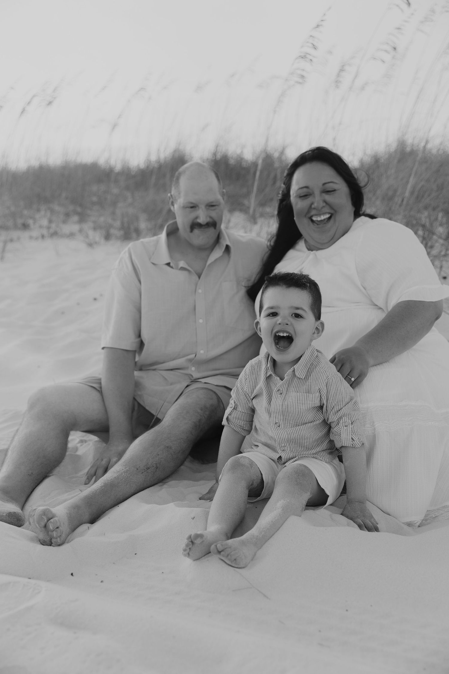 Black and white beach portraits showing a family sitting together in the sand, progressing through different candid poses.