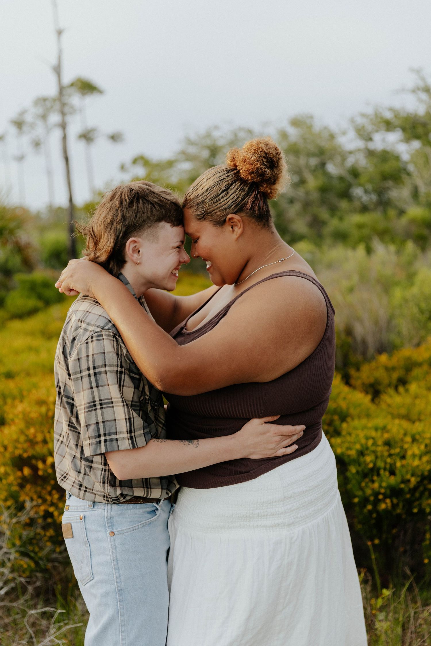 Two people share an intimate embrace outdoors among blooming yellow wildflowers.