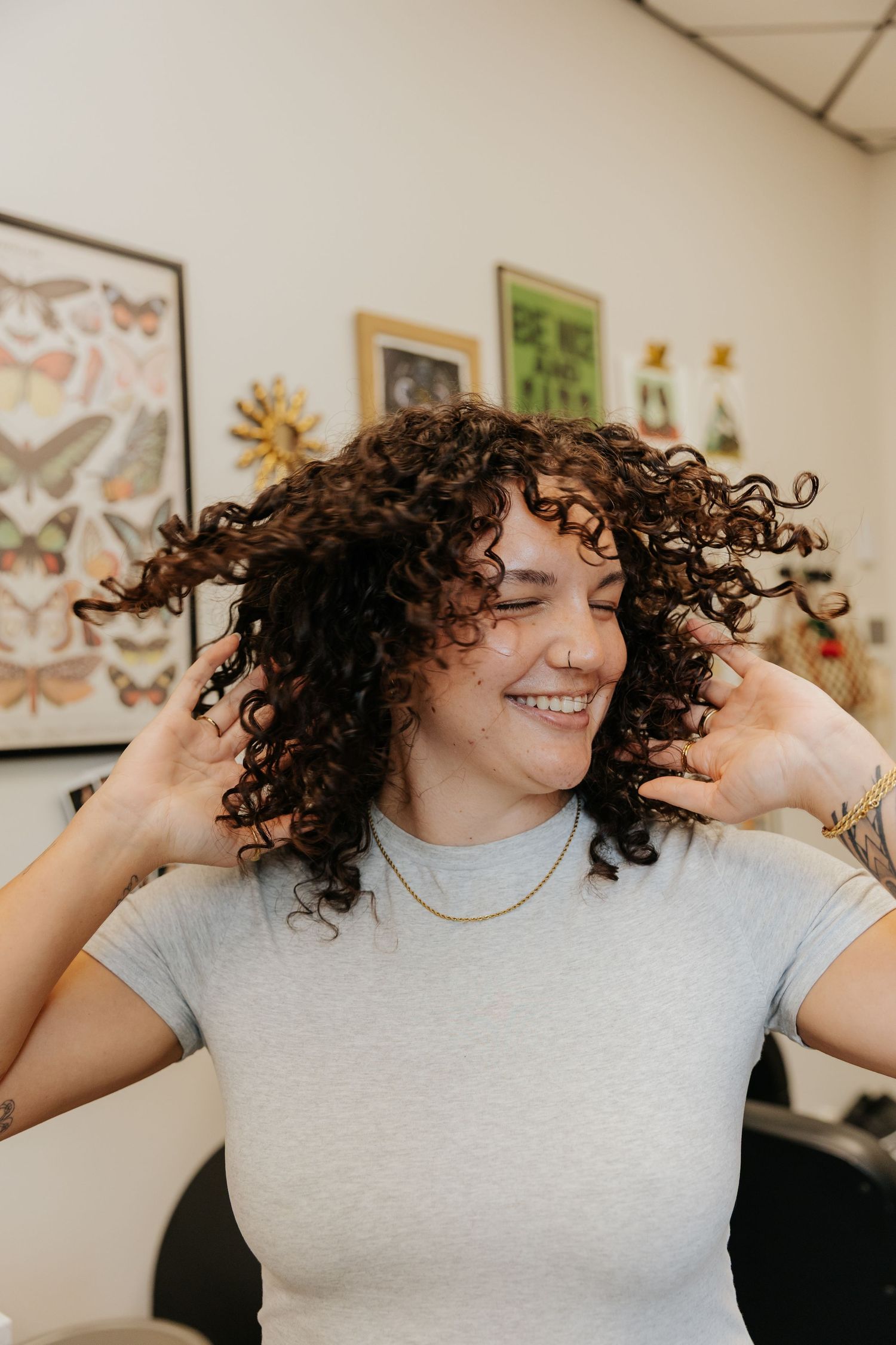 Three sequential photos show someone with curly hair playfully flipping and tossing their natural curls in a gray t-shirt.