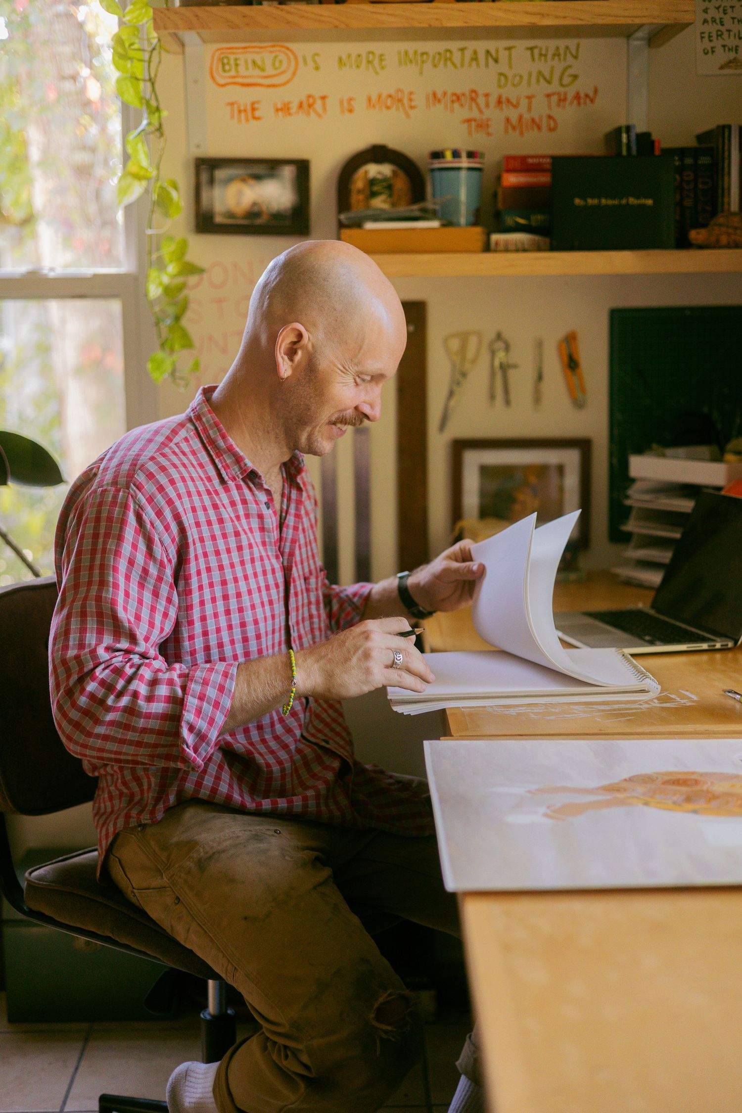 A series of photos showing someone in a pink checkered shirt working at a wooden desk in a sunlit office space.