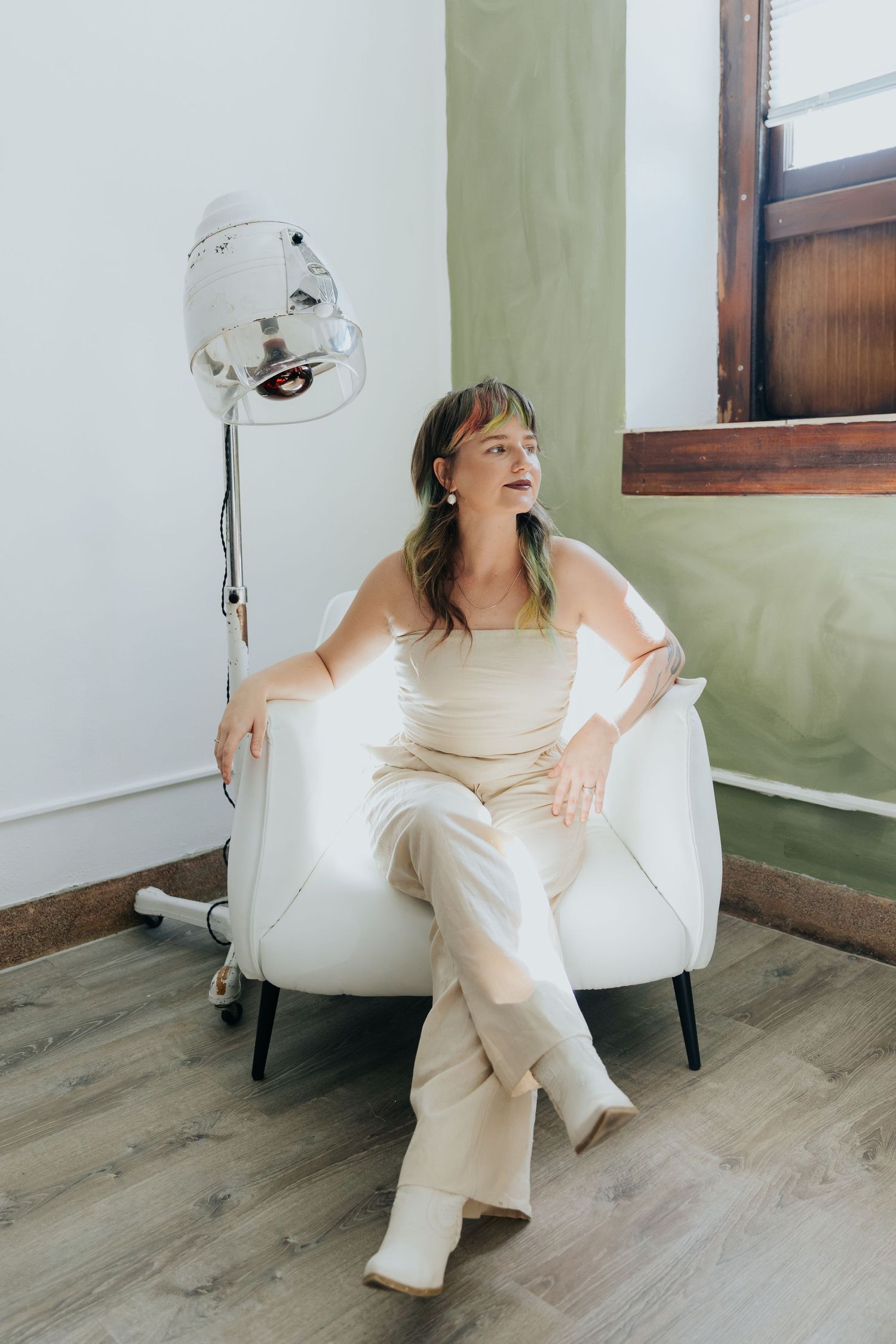 Person in white clothing lounges playfully on a modern chair against green walls in an interior setting.