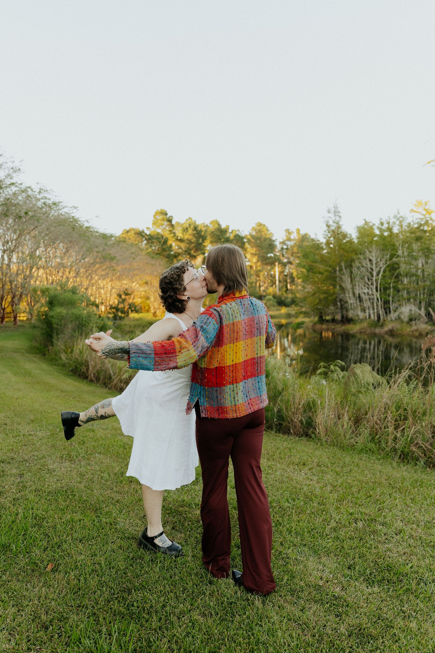 Two people in casual attire dance together on a grassy hillside during golden hour.