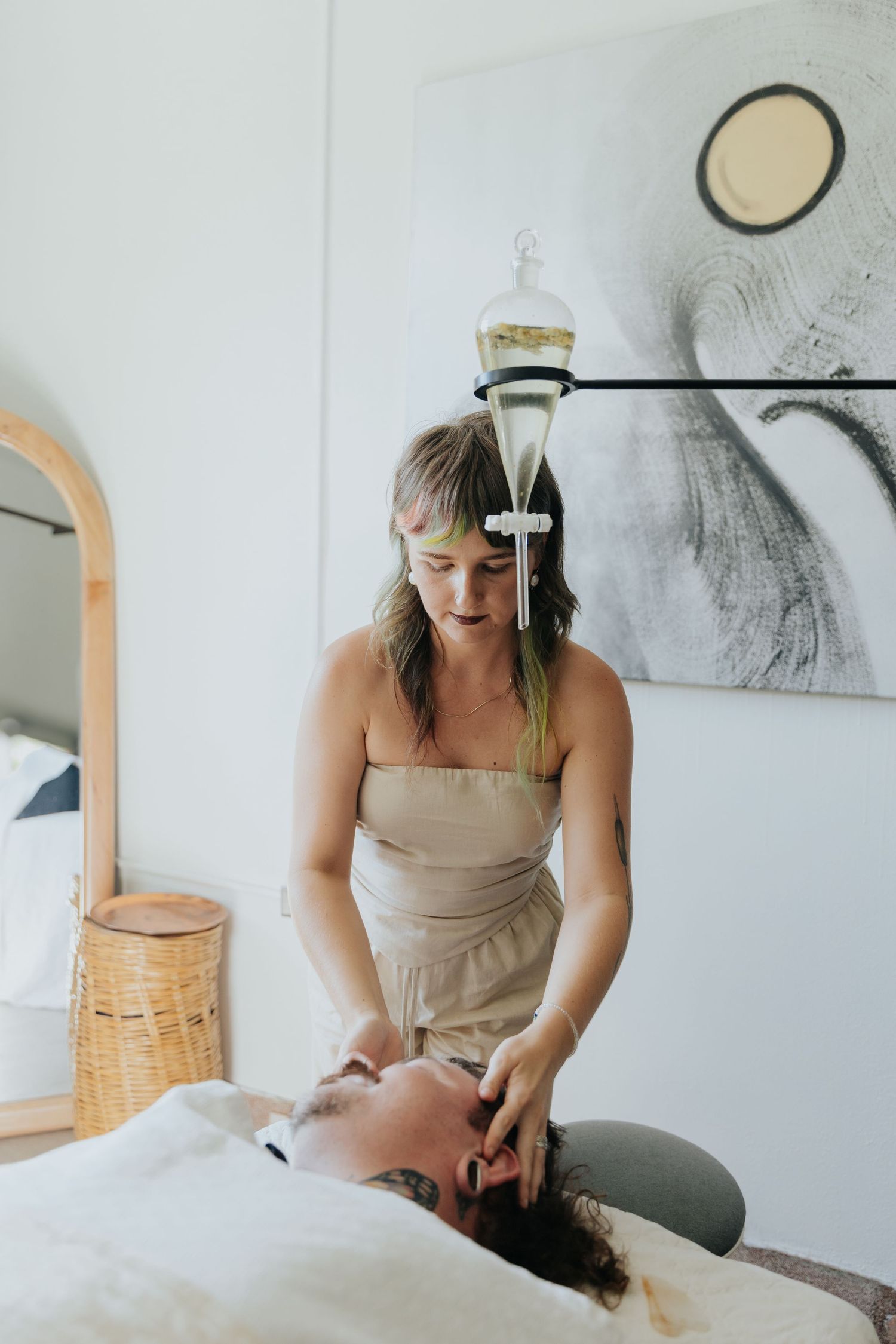 Massage therapist in beige apron performs facial treatment on client at wellness spa.