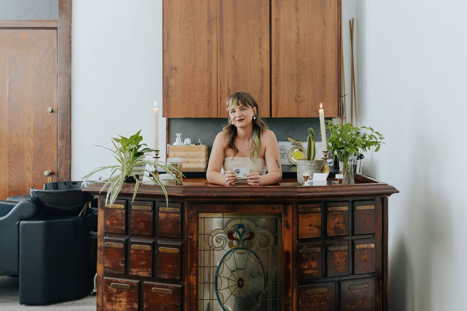 Someone sits at an ornate vintage wooden desk with plants in a bright minimalist room interior.