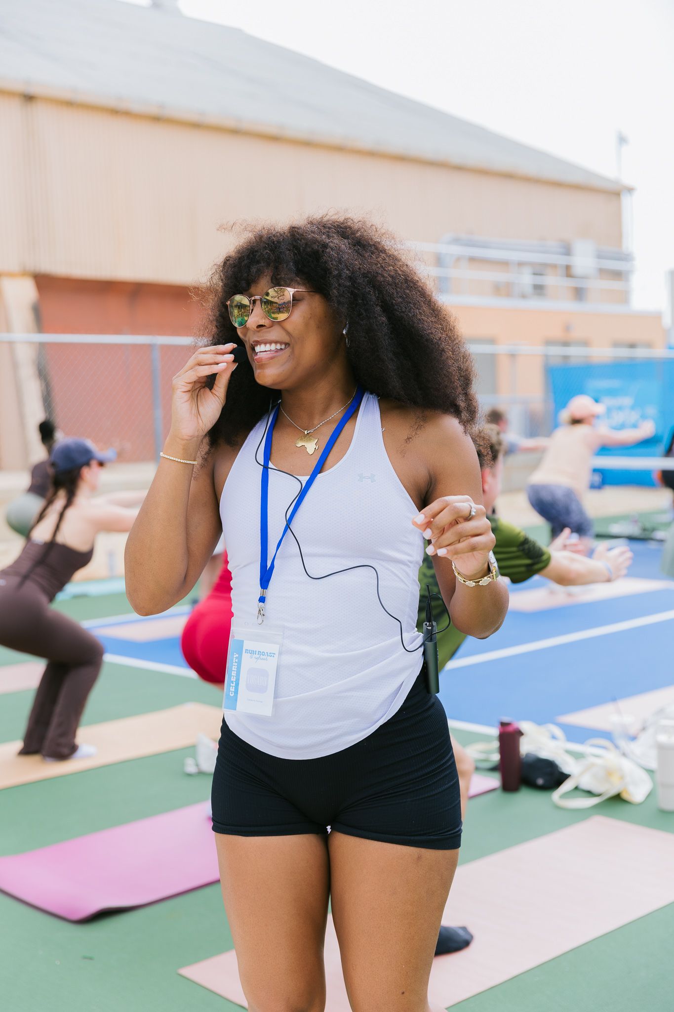 A person in athletic wear smiles and stretches during an outdoor fitness class on blue and green exercise mats.