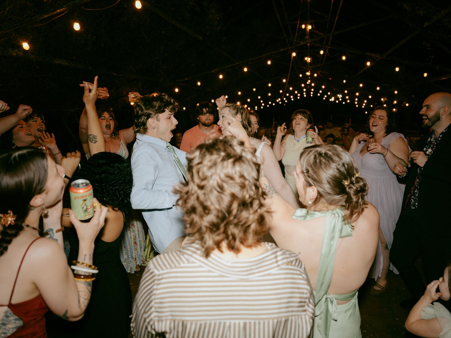 Guests dancing outdoors at night under string lights at a lively wedding reception party.
