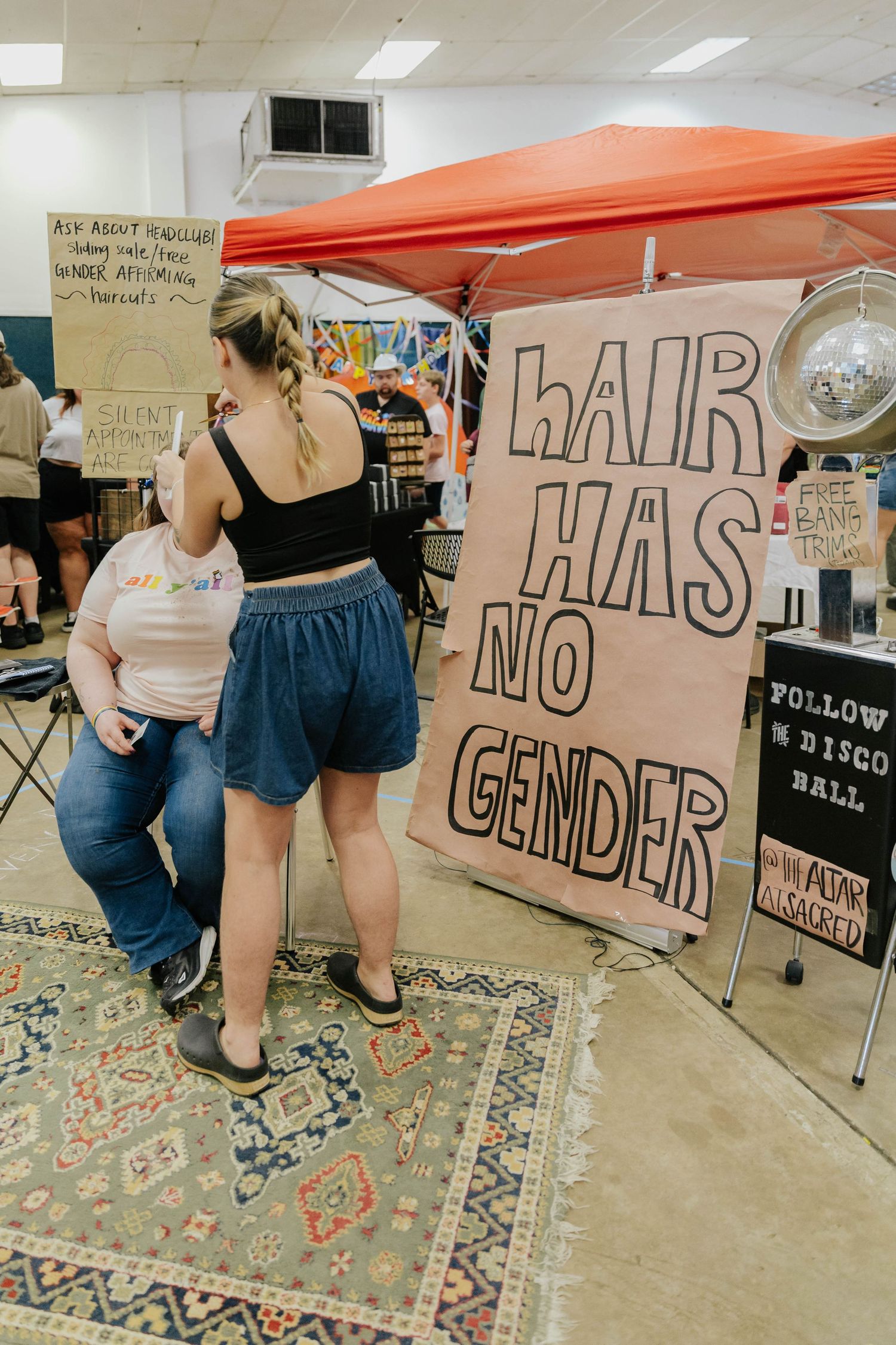 Indoor event space with orange tent and decorative sign about hair displayed on patterned area rug.