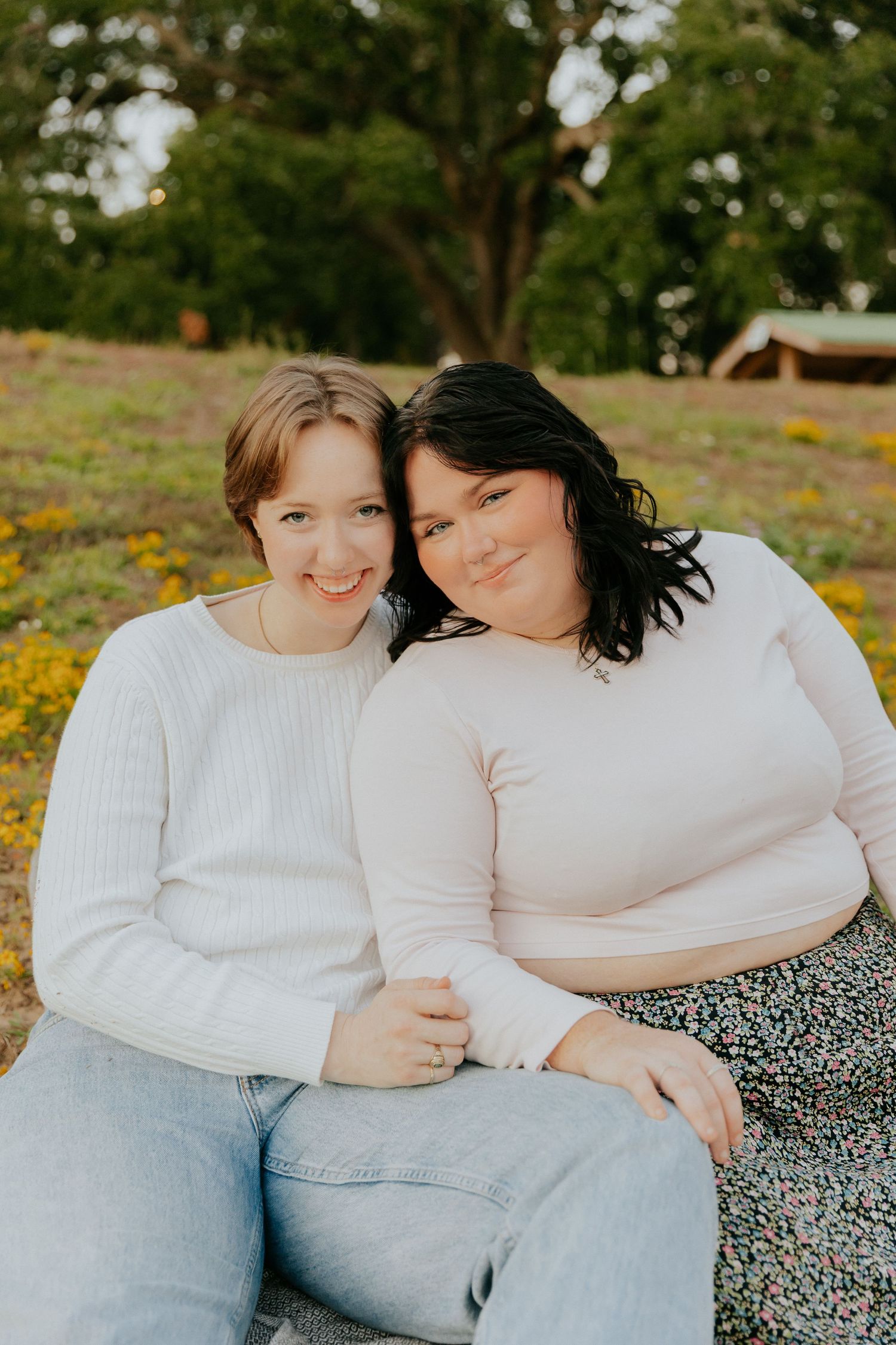 Two people in light colored tops share intimate moments while sitting together in a field of yellow wildflowers.