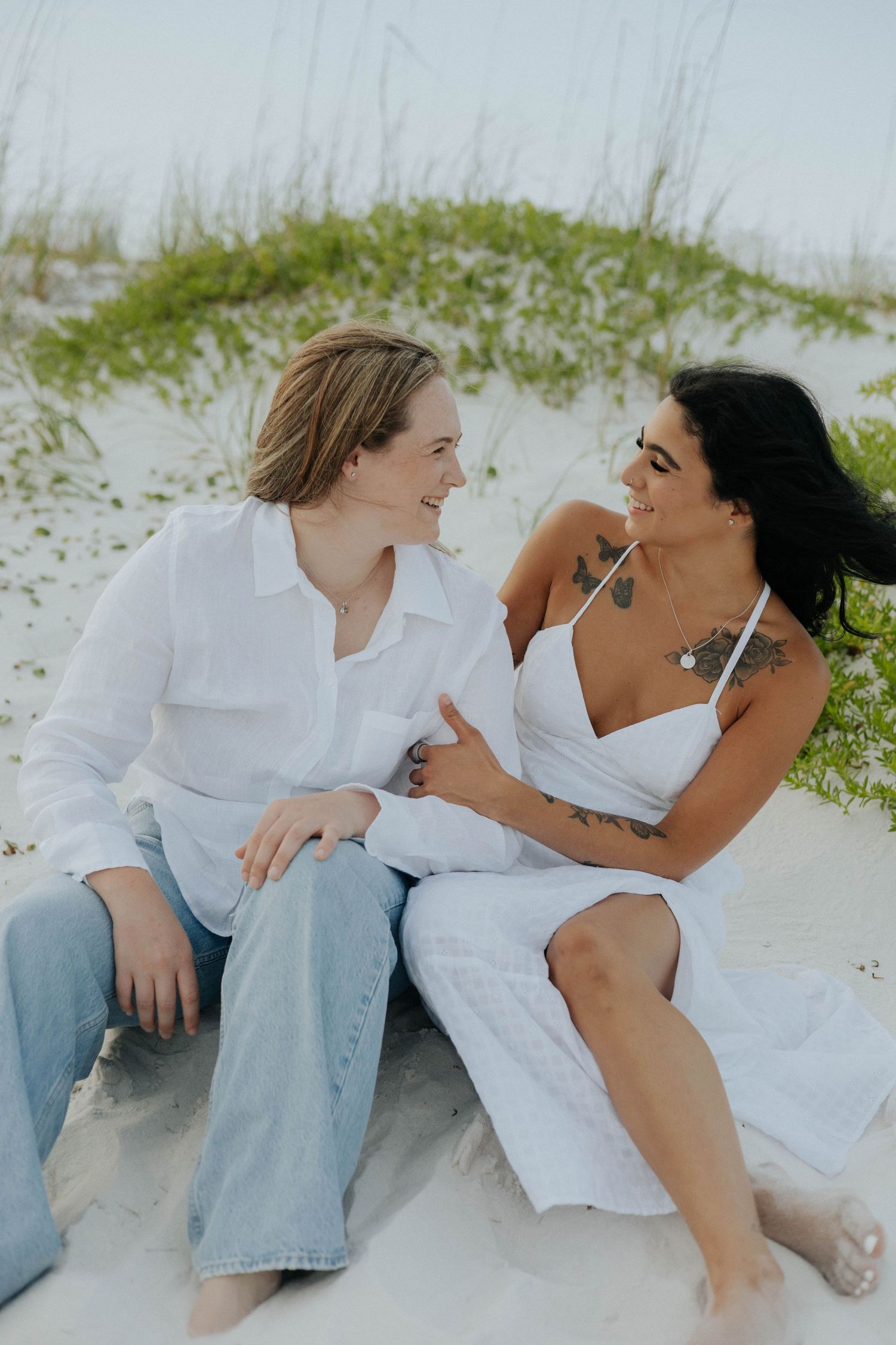 A couple in white clothing shares intimate moments while relaxing together on a sandy beach.