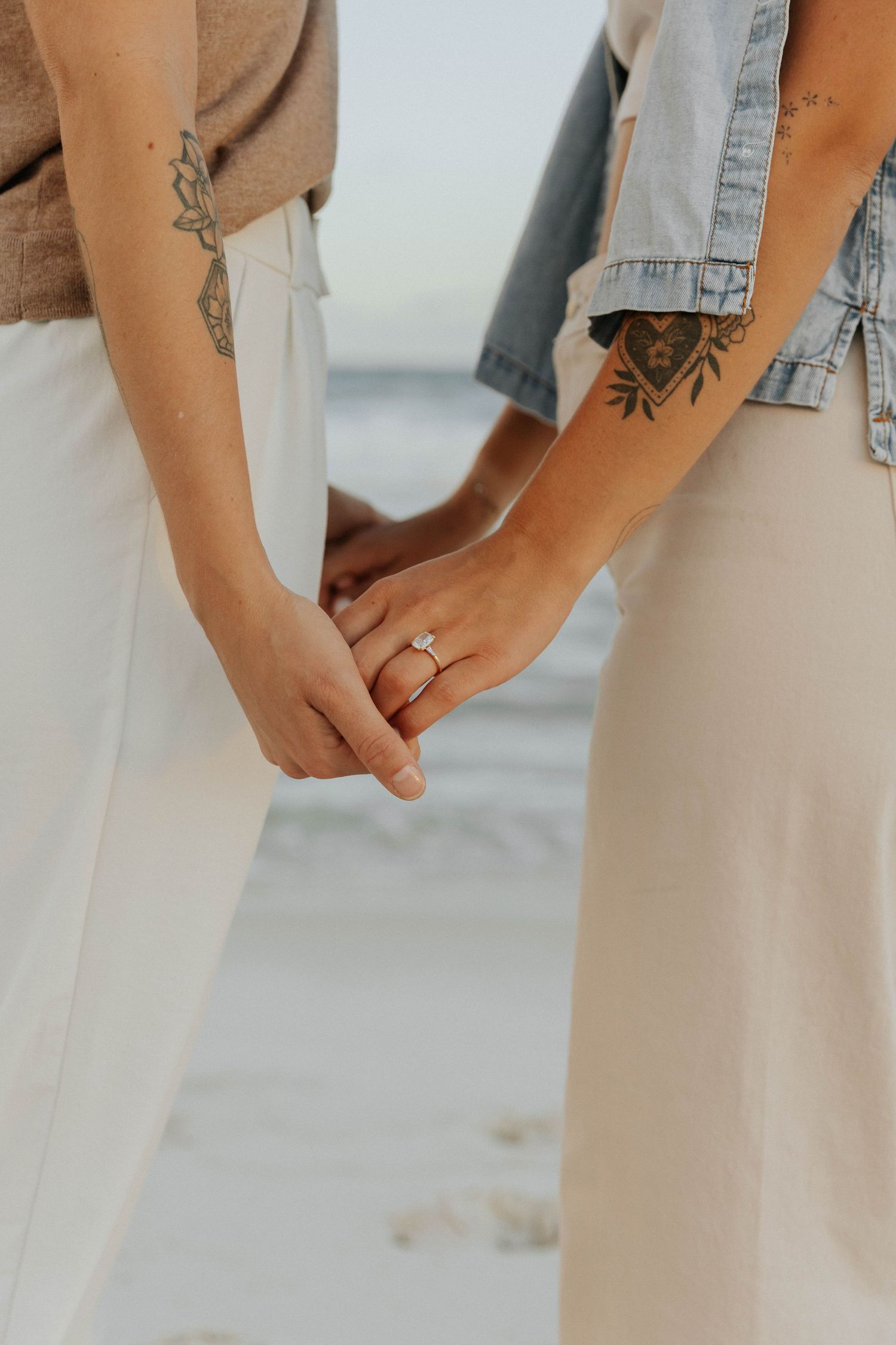 Close-up view of hands wearing a denim jacket and holding a delicate engagement ring against a light background.