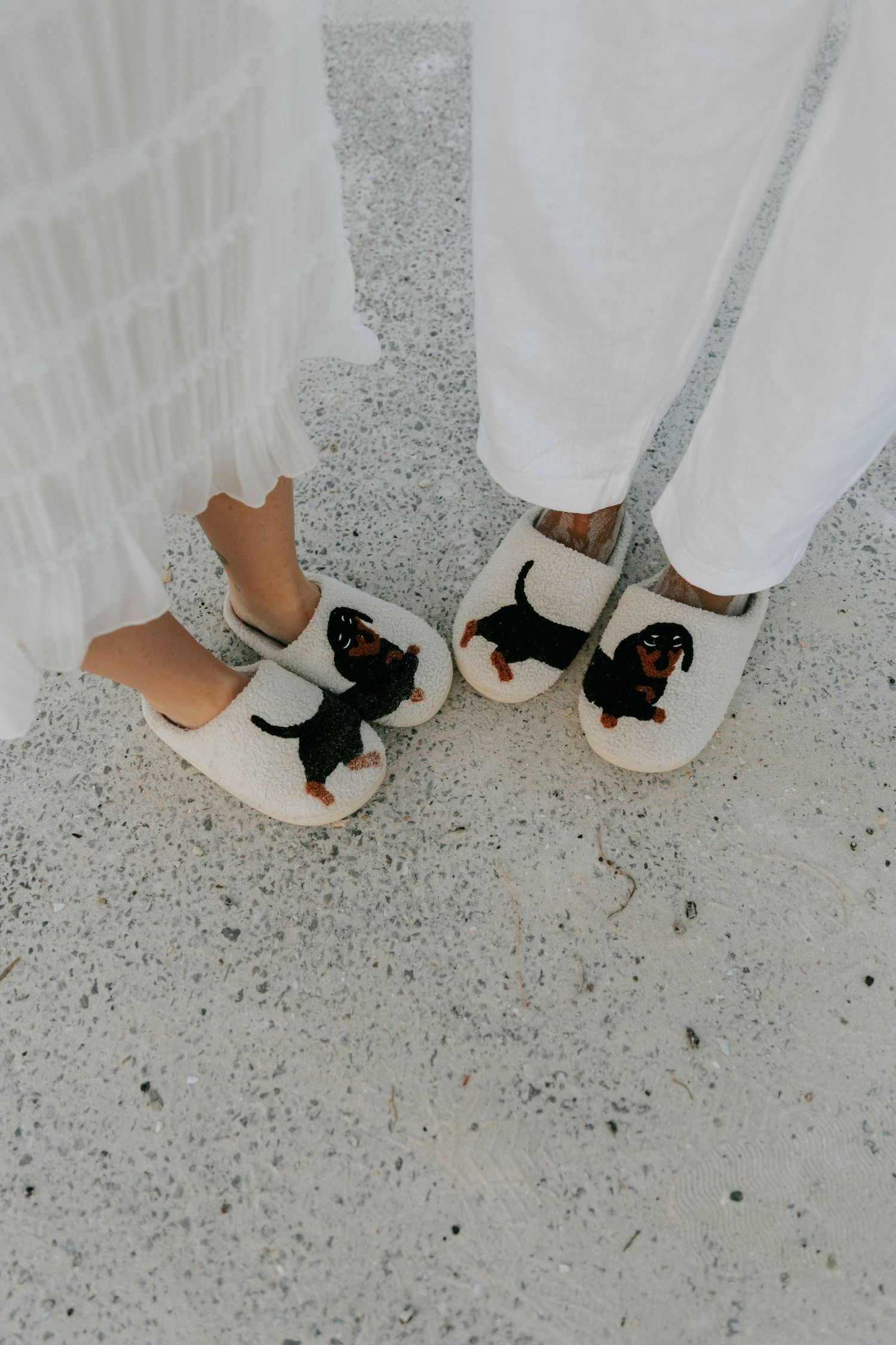 Three matching white shoes with black cat designs on them shown against a speckled gray floor surface.
