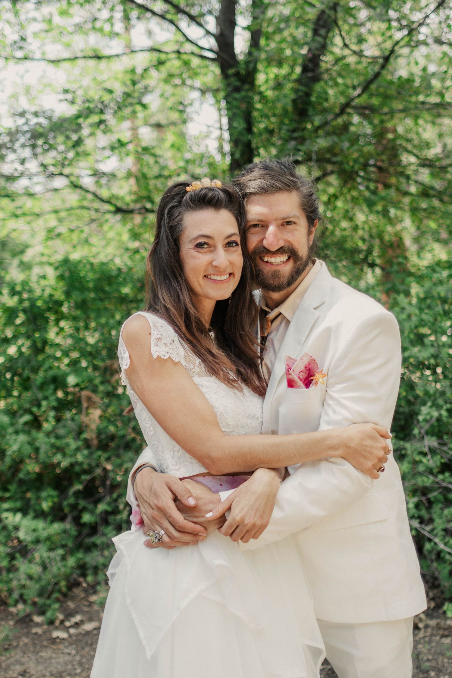 A couple shares joyful moments in their wedding attire against a lush green outdoor backdrop.