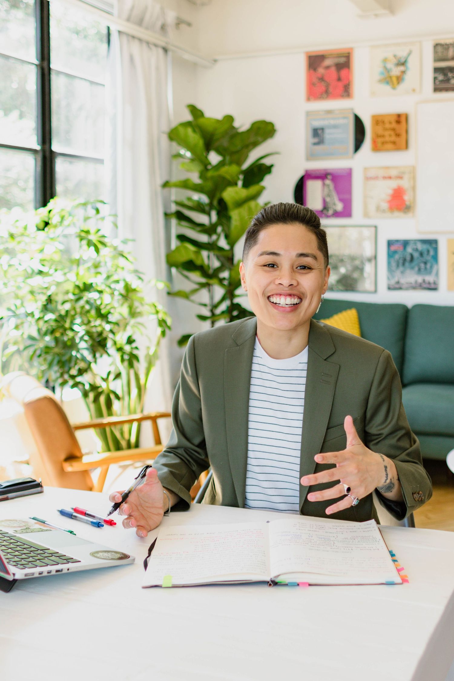 Professional working at bright modern desk with indoor plants and artwork displayed on walls in background.