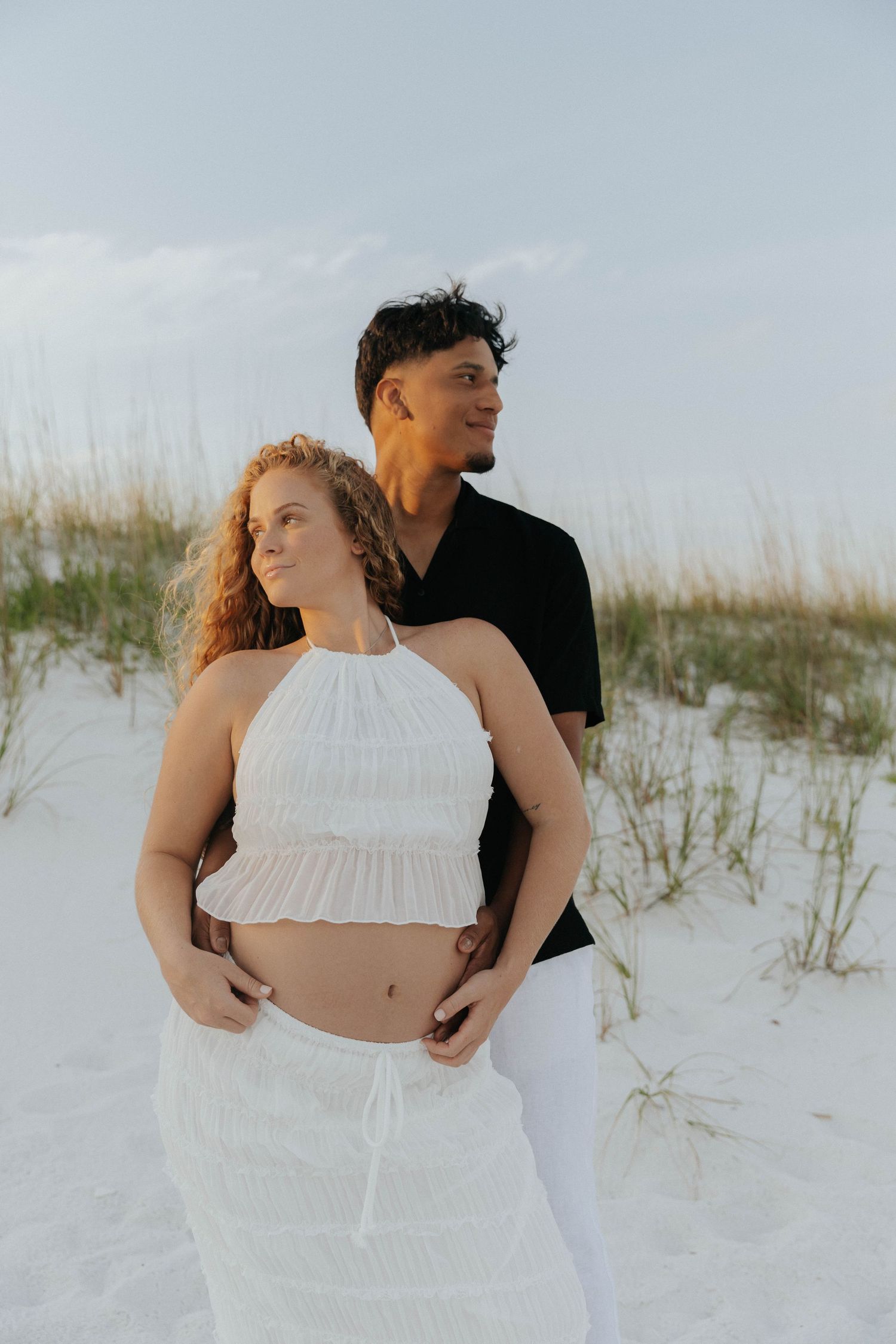 A couple embraces on a white sandy beach with sea grass in the background during a romantic photoshoot.