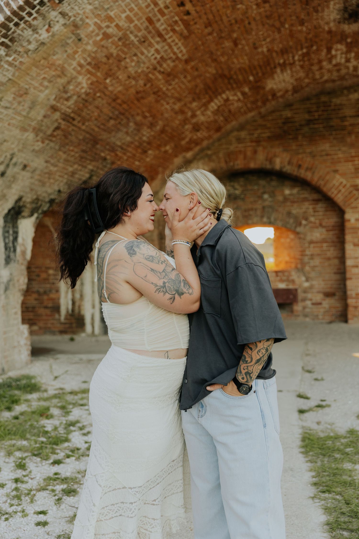 A romantic wedding couple shares intimate kisses in a rustic brick archway setting during their photo session.