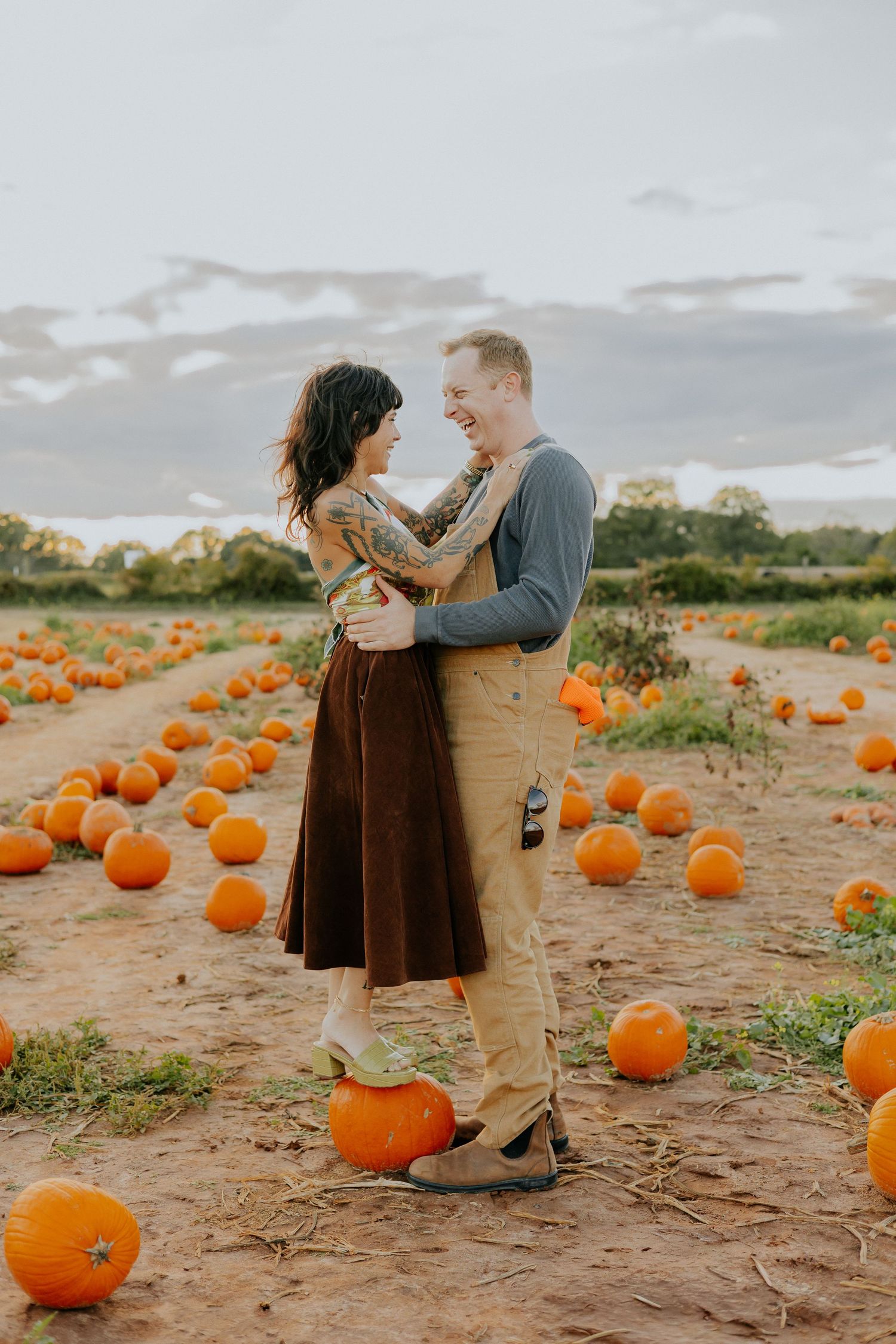 A couple shares a romantic moment in a pumpkin patch during autumn as orange pumpkins dot the ground around them.
