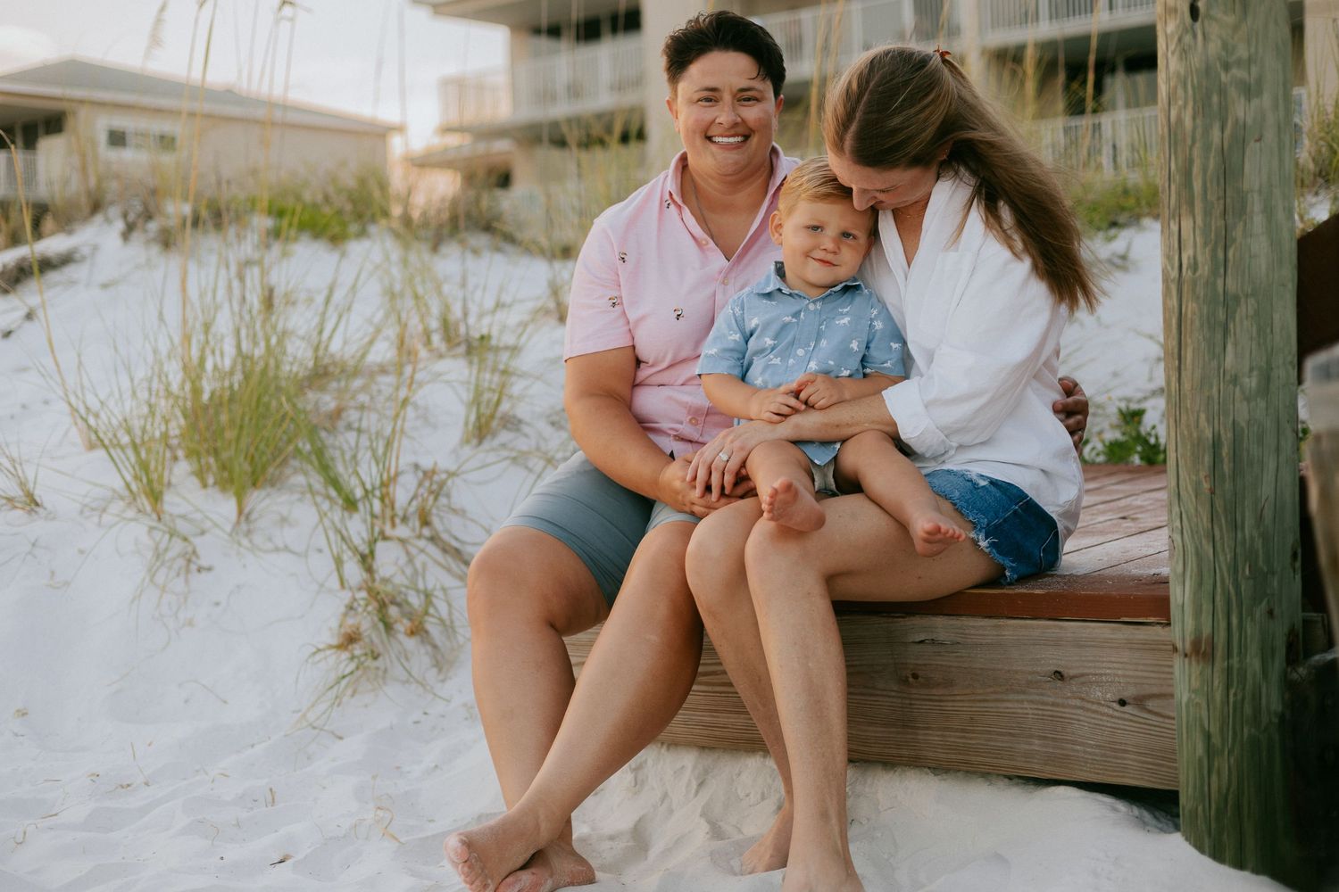 Family enjoying a sunny day together on a wooden boardwalk at the beach with white sand in the background.