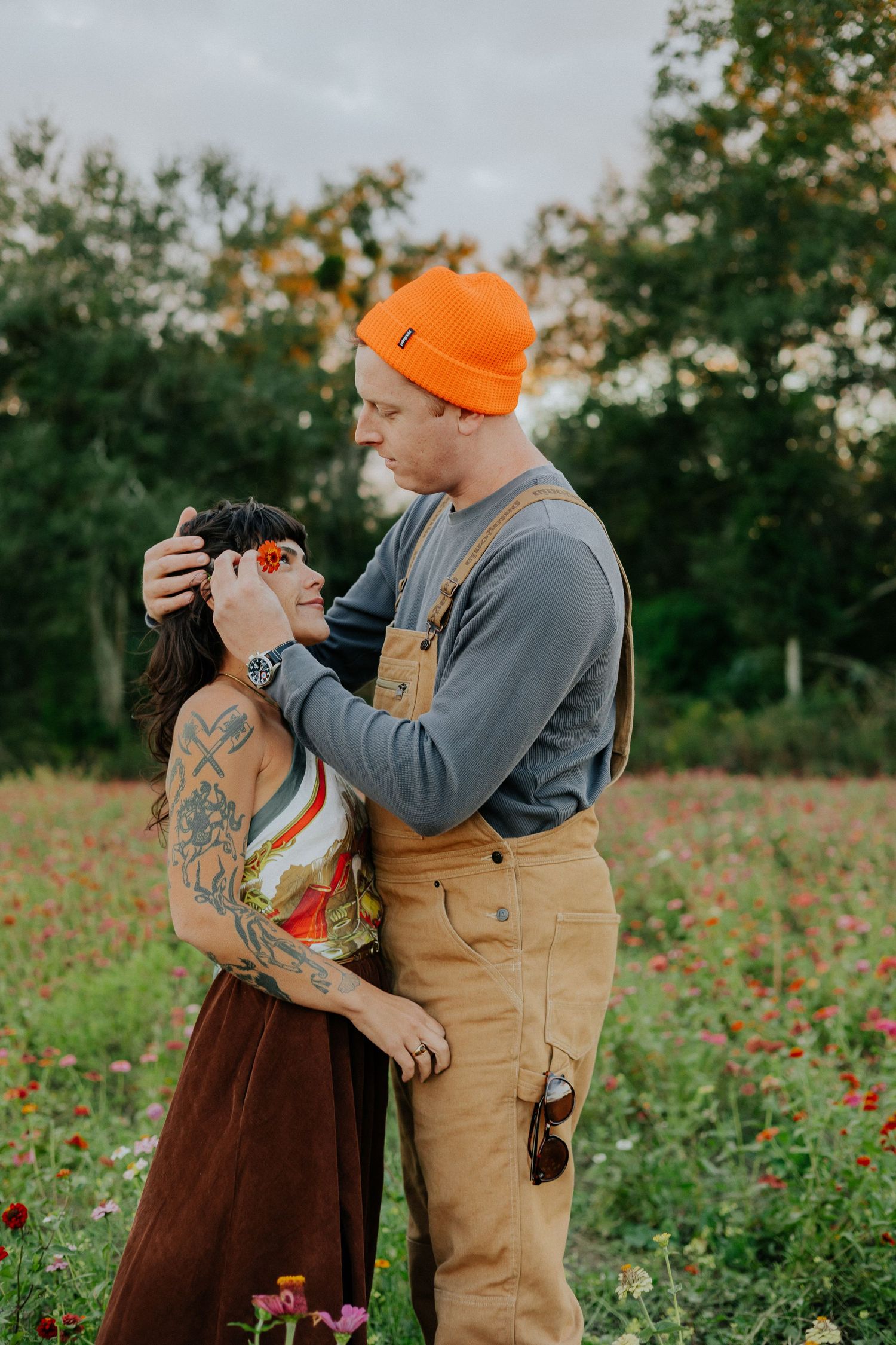 Couple in casual autumn attire sharing a tender moment in a field of red flowers.