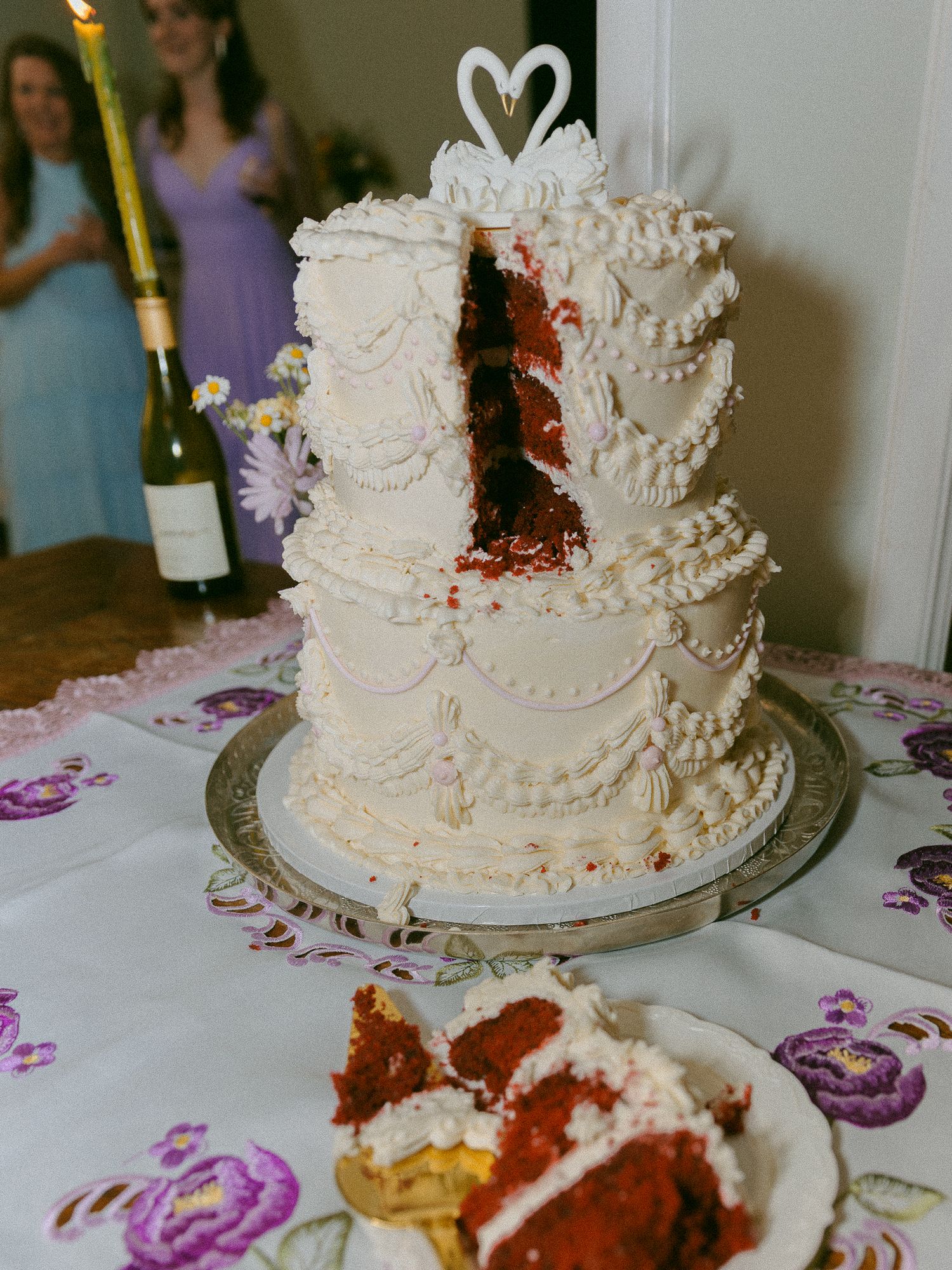 Three-tier red velvet wedding cake with white frosting and swan topper, partially cut to reveal red interior layers.