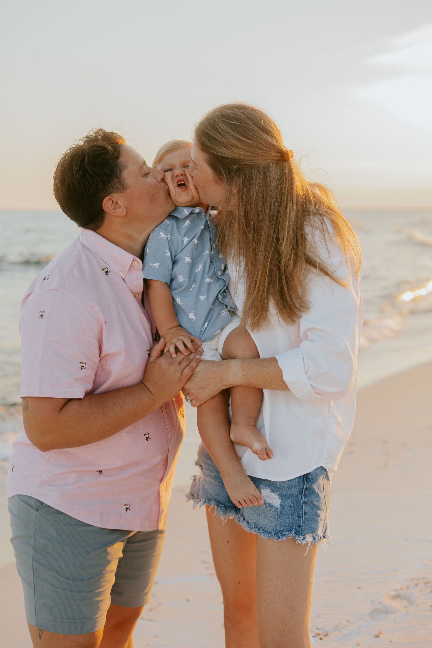 A romantic couple shares tender moments together on a beach at sunset in coordinated casual outfits.