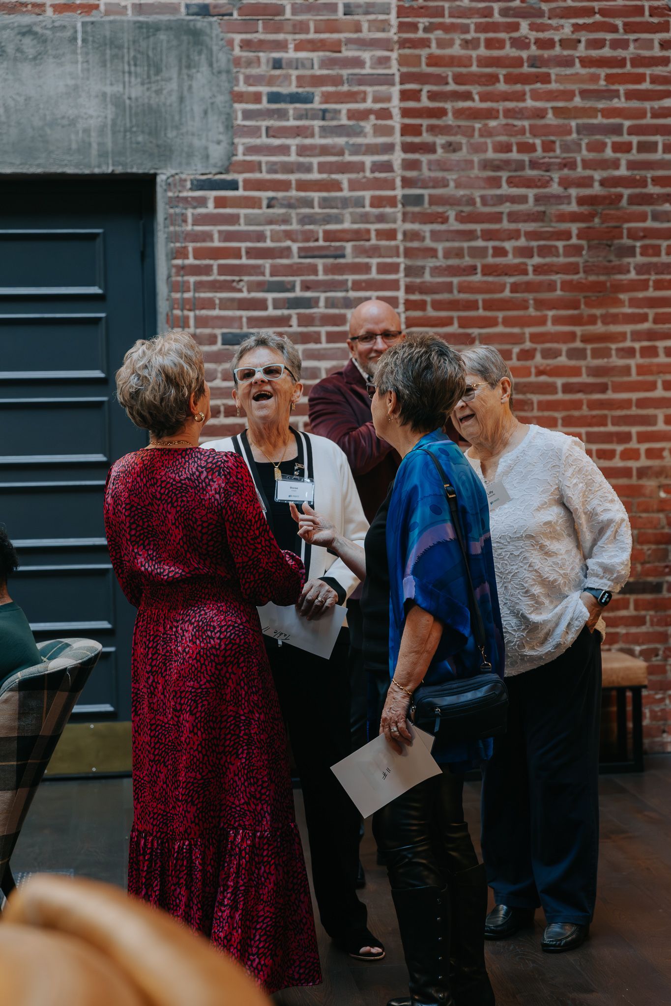 A group of people gather and interact in front of a brick wall at a social event.