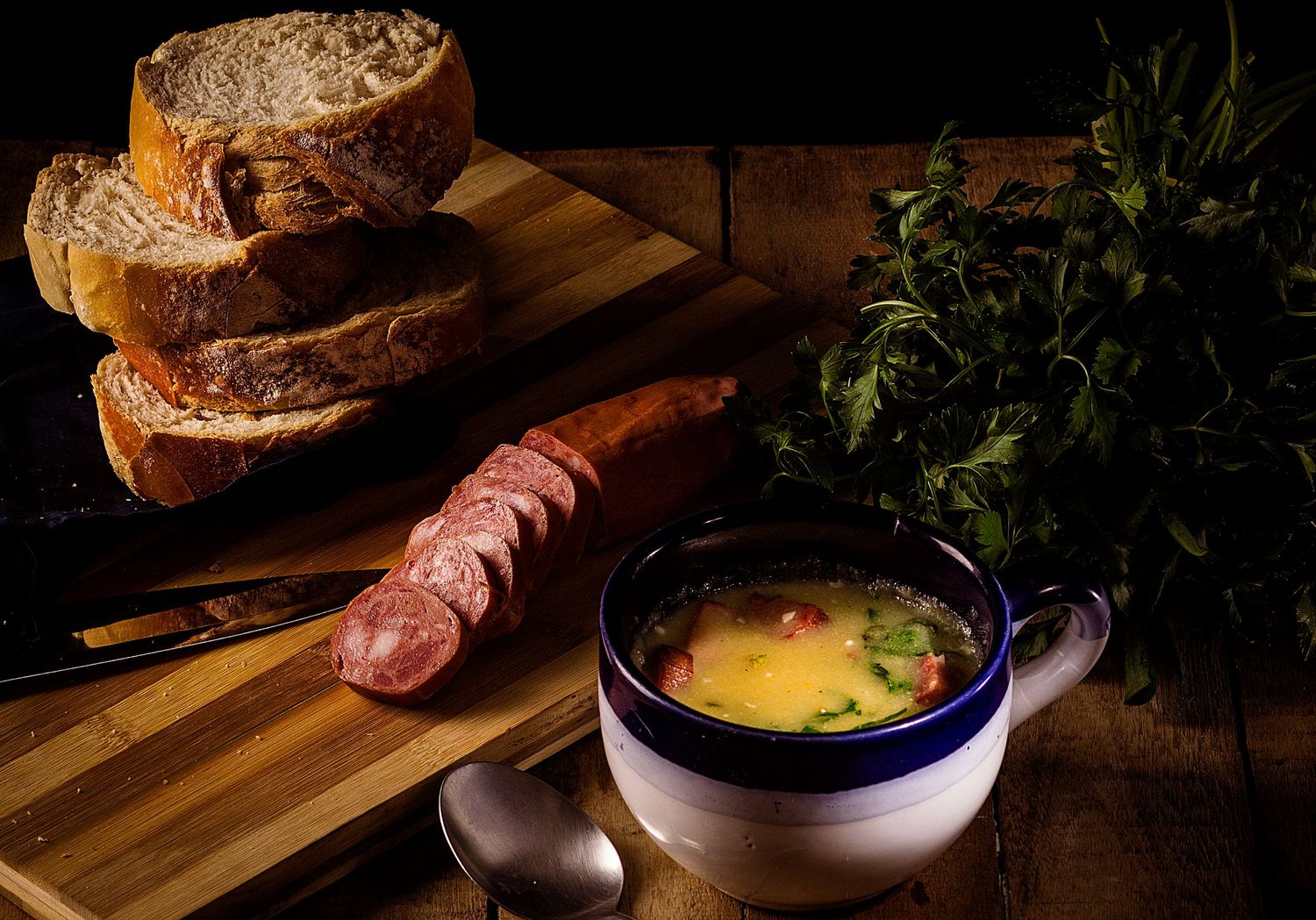 Sopa cremosa de mandioquinha com linguiça, pão rústico e cheiro-verde. Conforto e sabor em uma cena acolhedora.