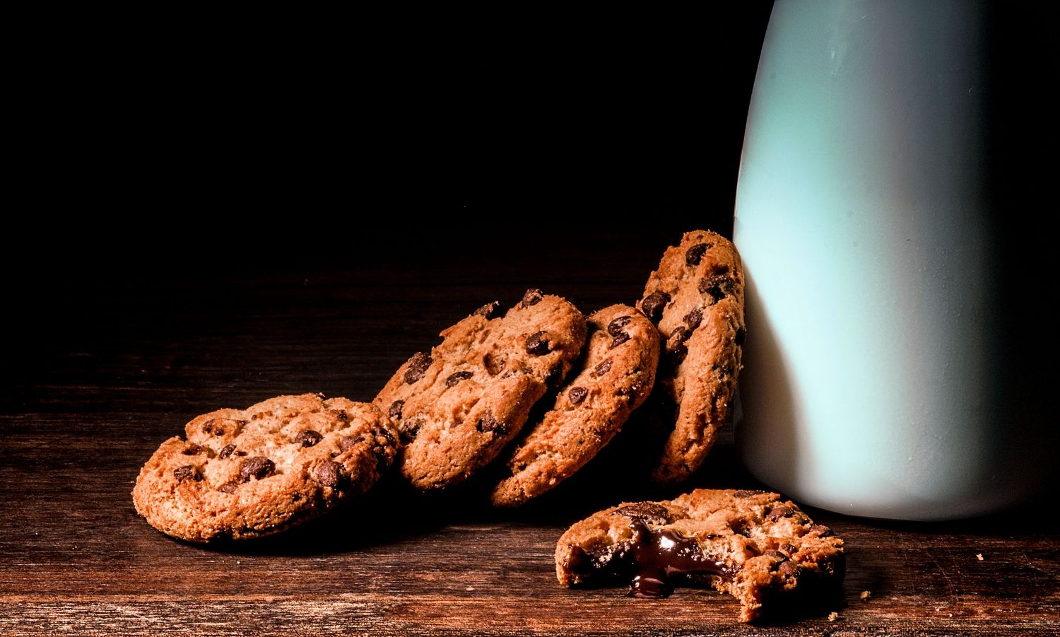 Cookies com gotas de chocolate e interior derretido, prontos para serem mergulhados em um copo de leite gelado.