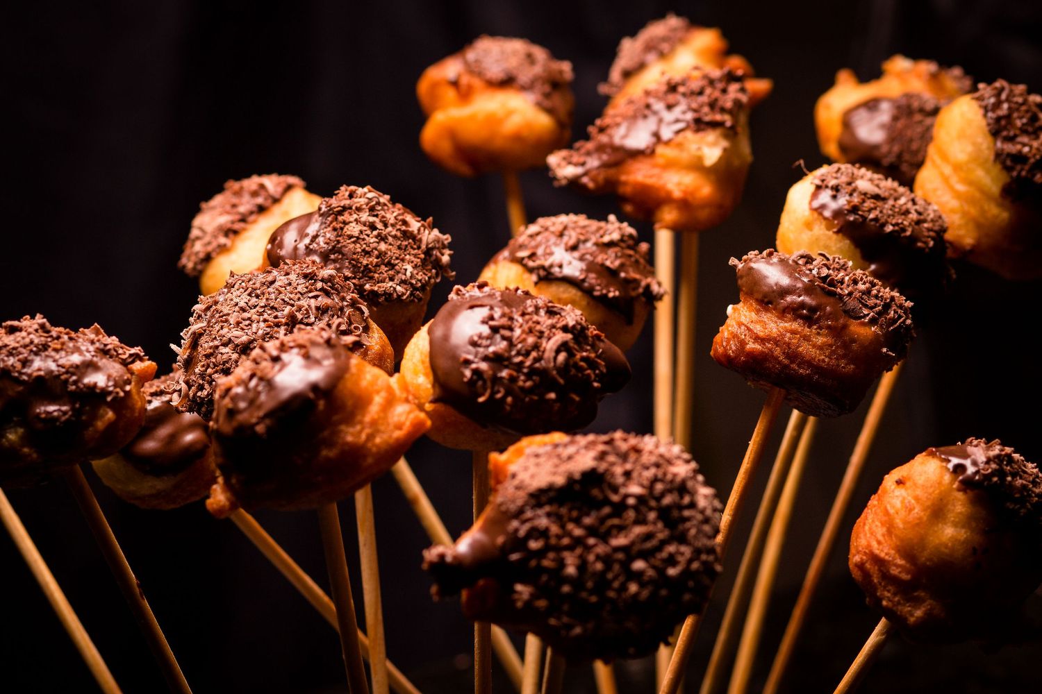 Bolinho de chuva, mergulhado em chocolate e coberto com raspas — luz e textura que despertam desejo em cada detalhe.