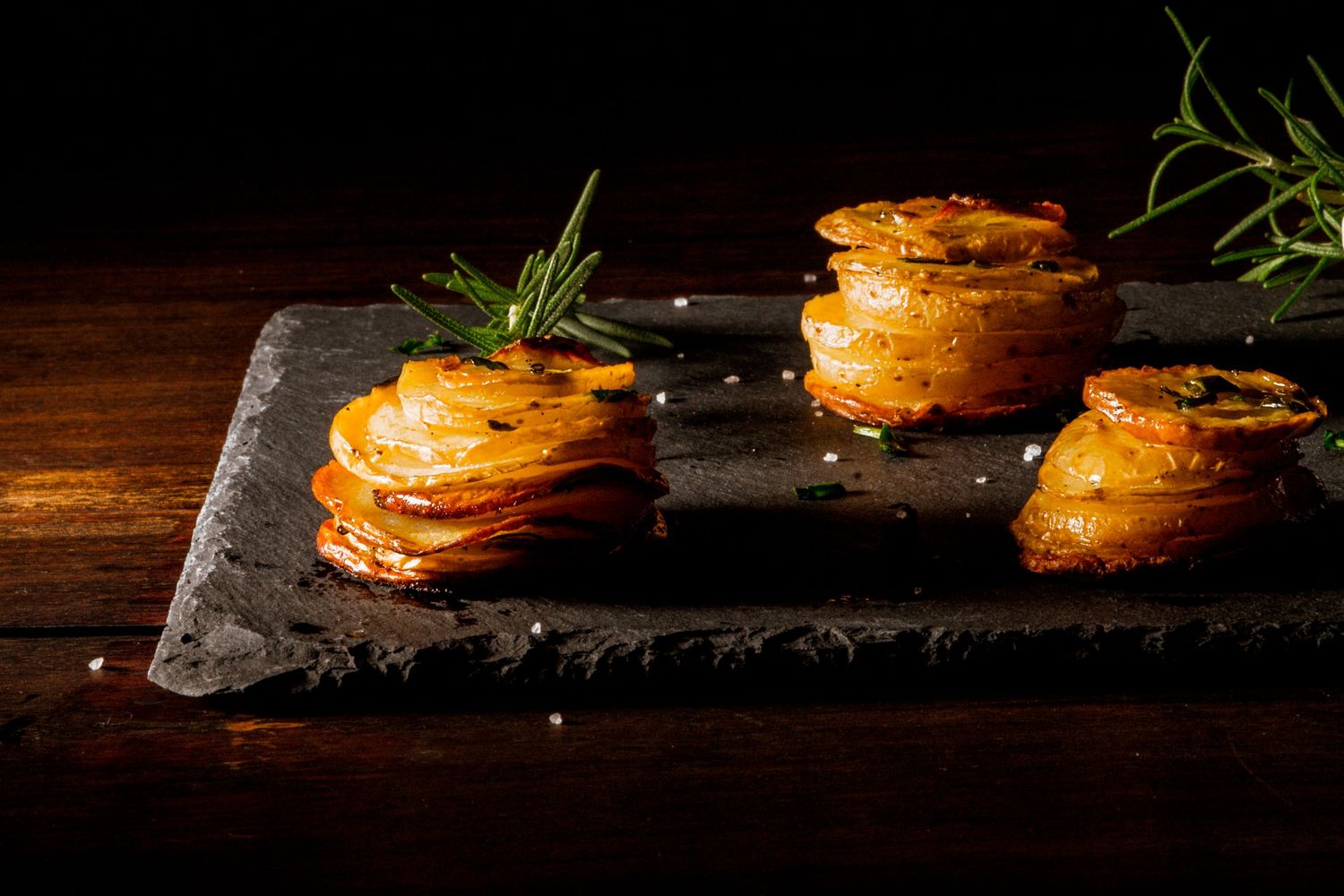 Batatas finamente laminadas, assadas até ficarem douradas e crocantes, finalizadas com flor de sal e ramos de alecrim.