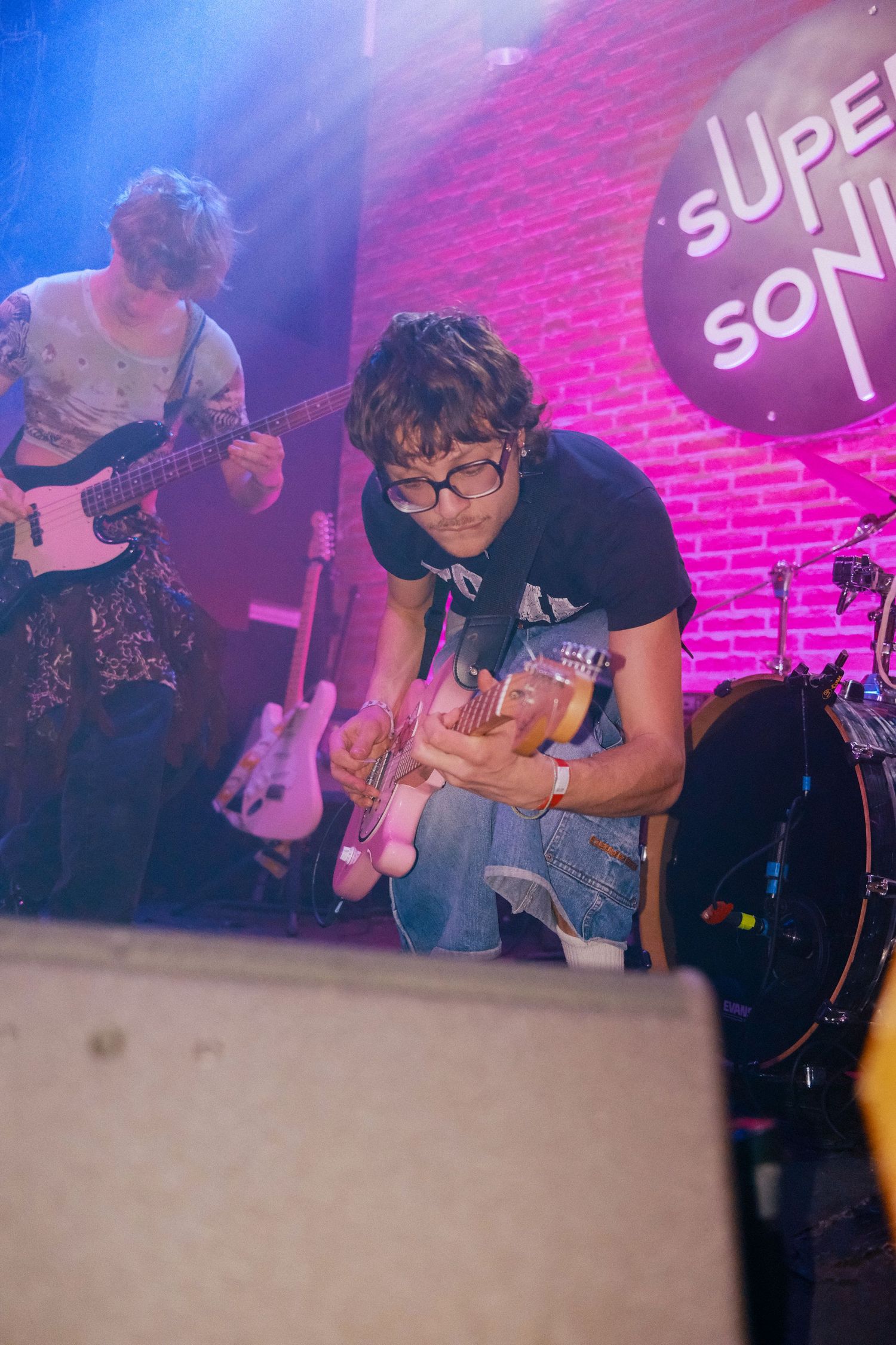 2 guitaristes jouent de la guitare sur la scene du Supersonic, les lumières sont violetas, et ils ont un look alternatif