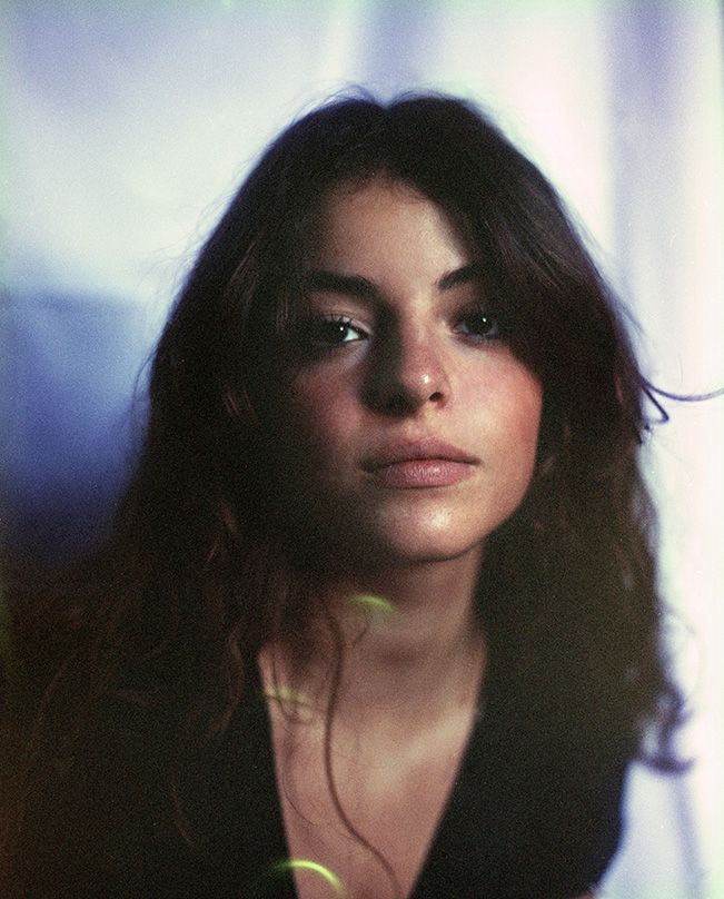 portait de Camille riche, de près, expression de visage naturelle, douce et chaleureuse sur un fond bleuté