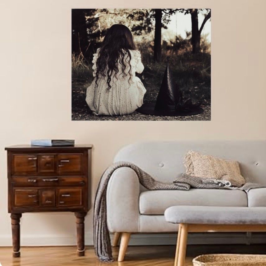 Canvas wall art of a girl with long hair sitting in a forest with a witch hat beside her. Available to purchase.