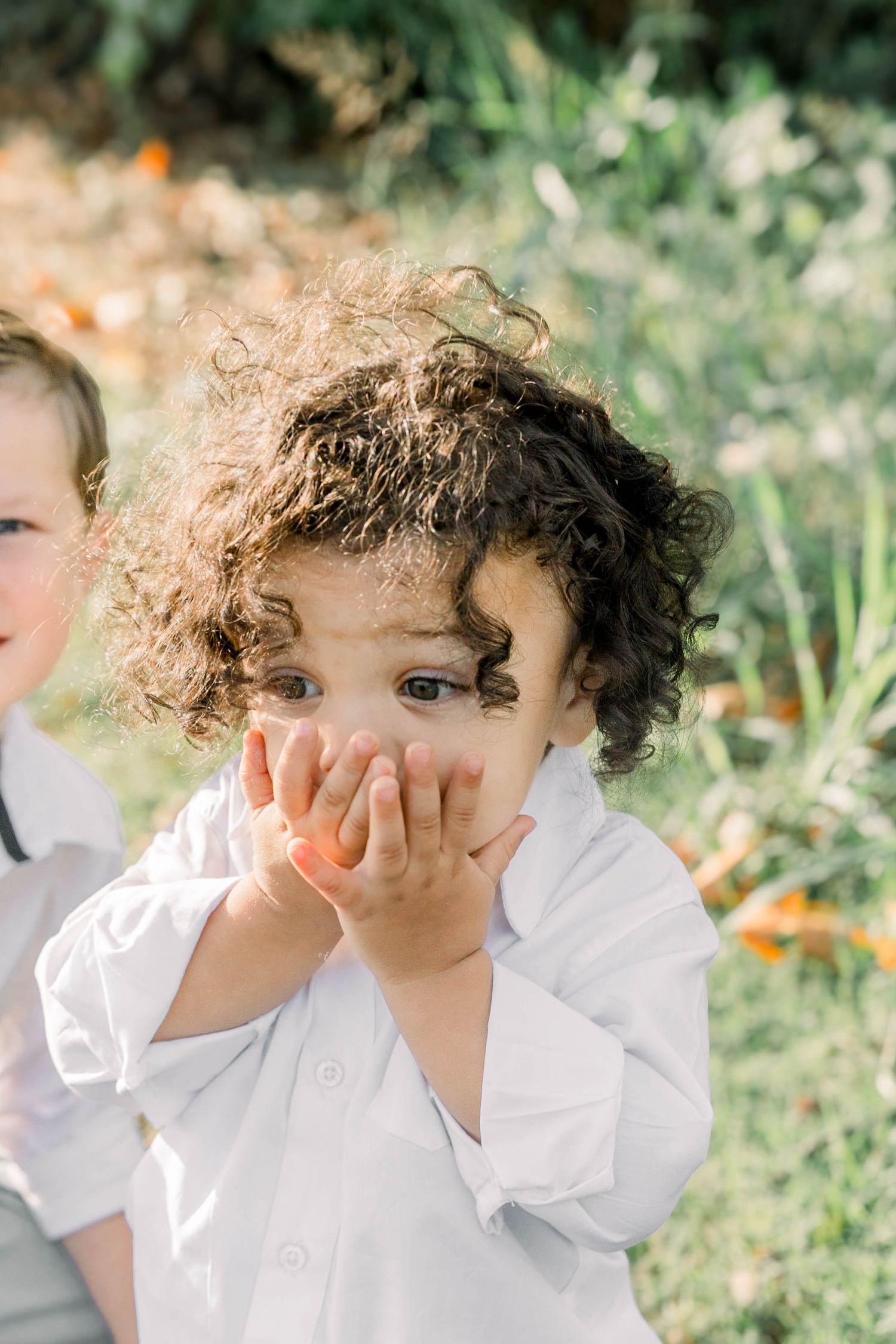 Close-up shots of curly-haired child in white shirt playing peek-a-boo outdoors.