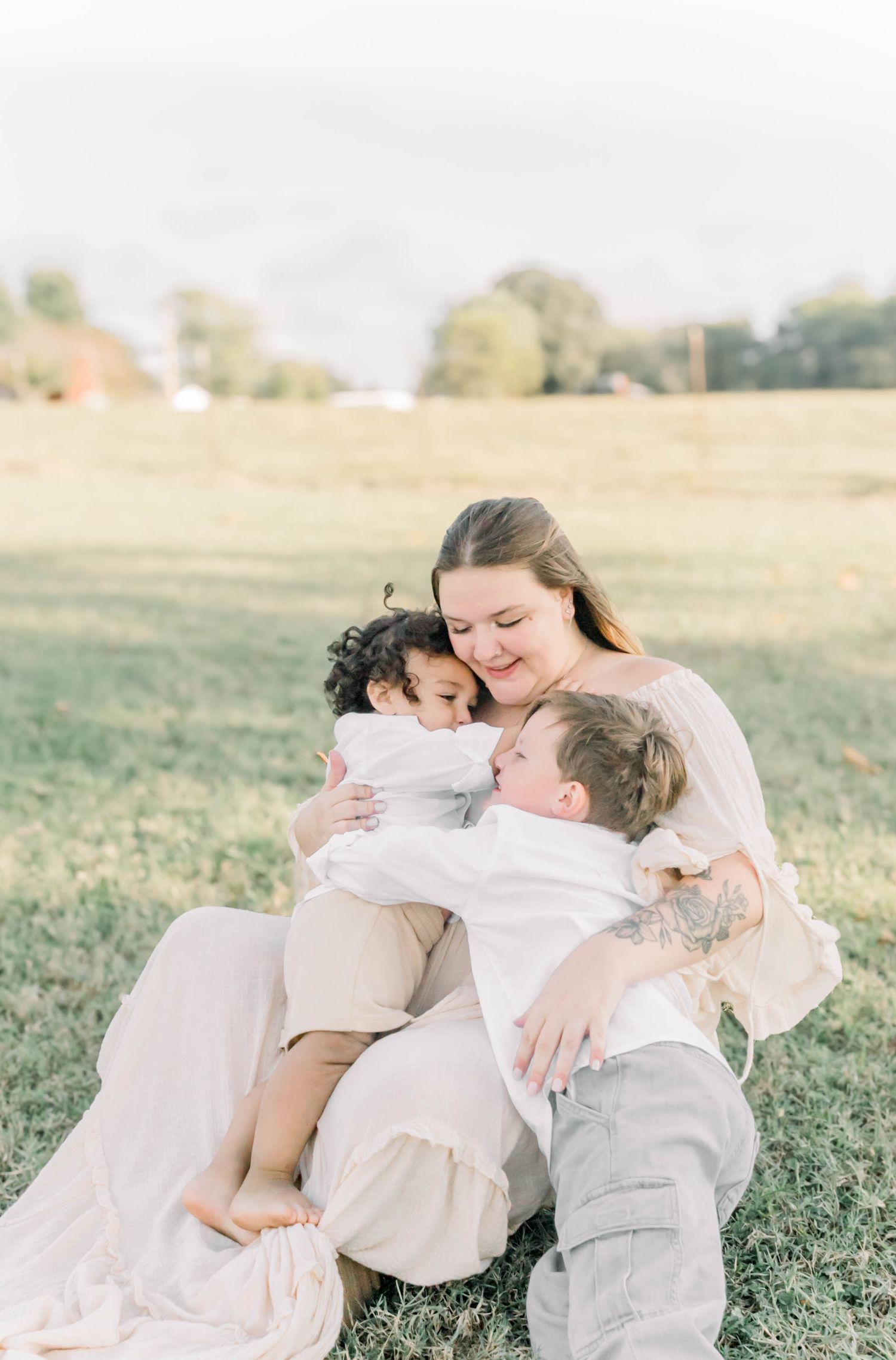 A tender family embrace in a sunlit field wearing light colored clothing.
