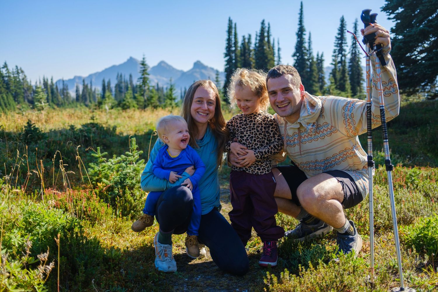 Group photo on a scenic mountain trail with evergreen forest and peaks in the distance.