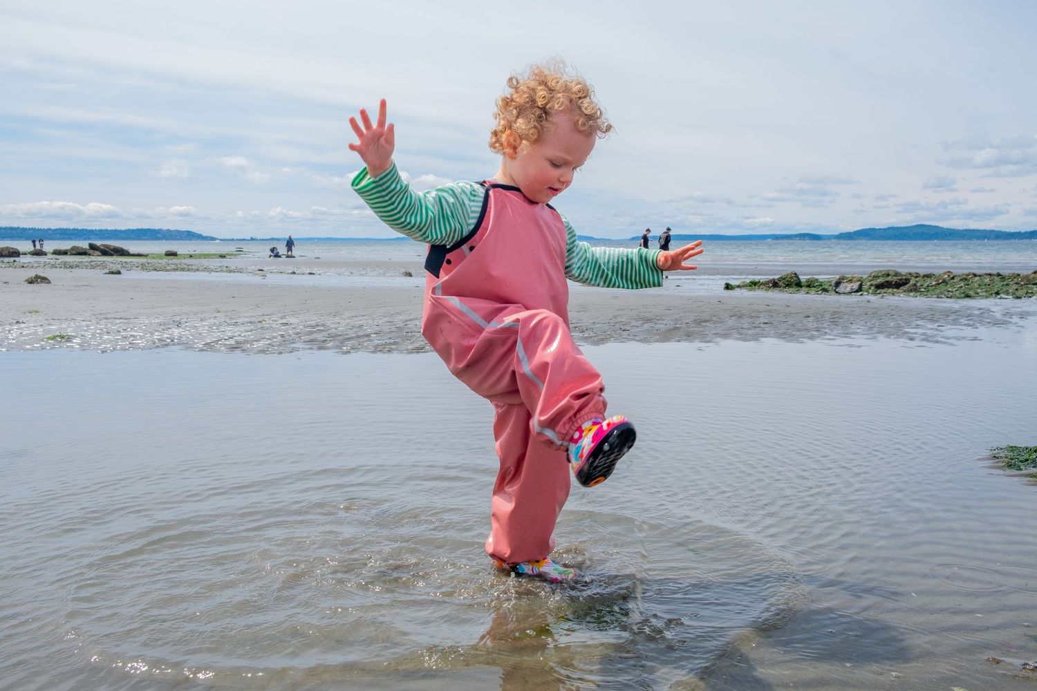 A sequence of photos showing a child in pink splashing and playing at the beach.