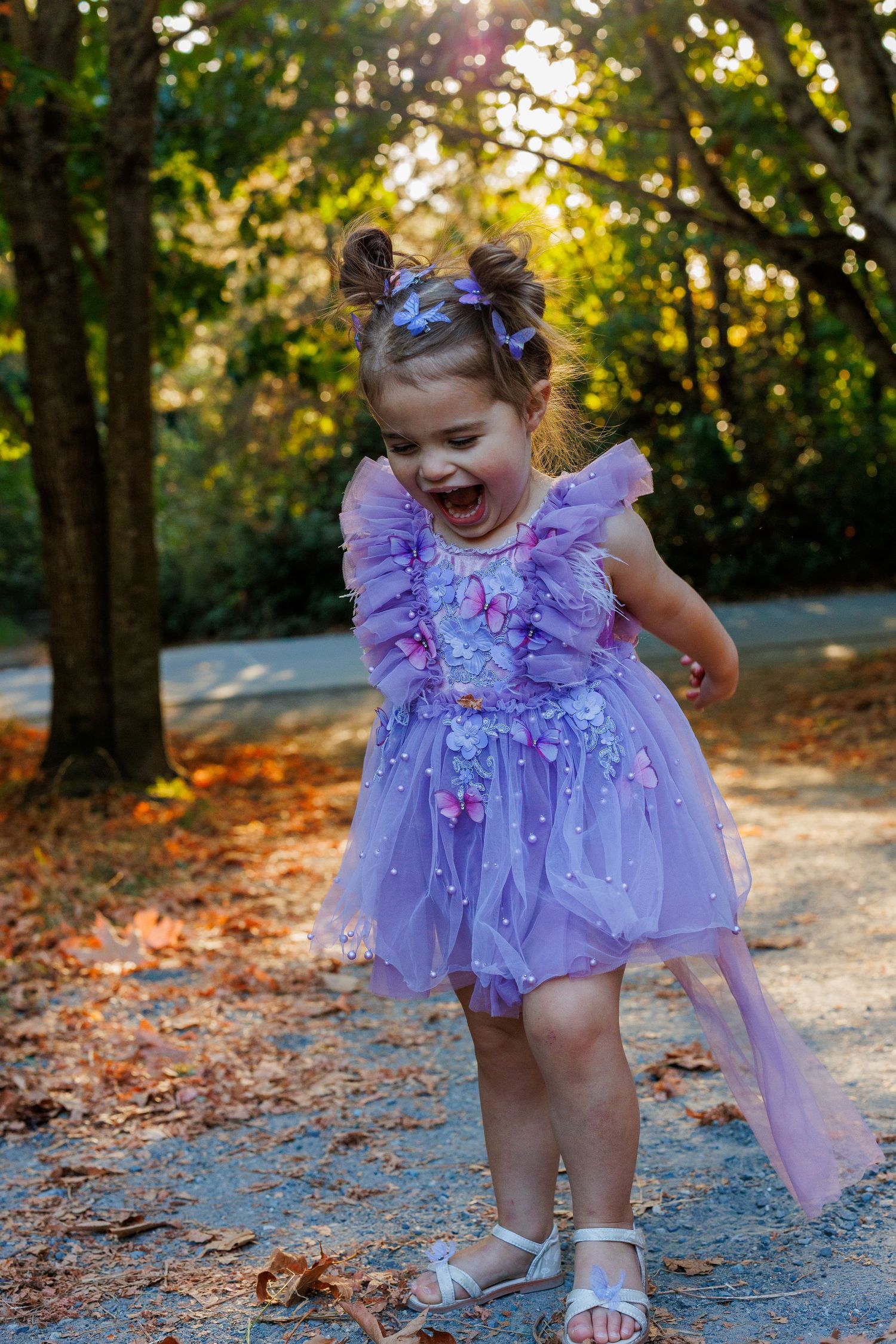 Playful moments captured on a leaf-covered path wearing a flowing purple dress.