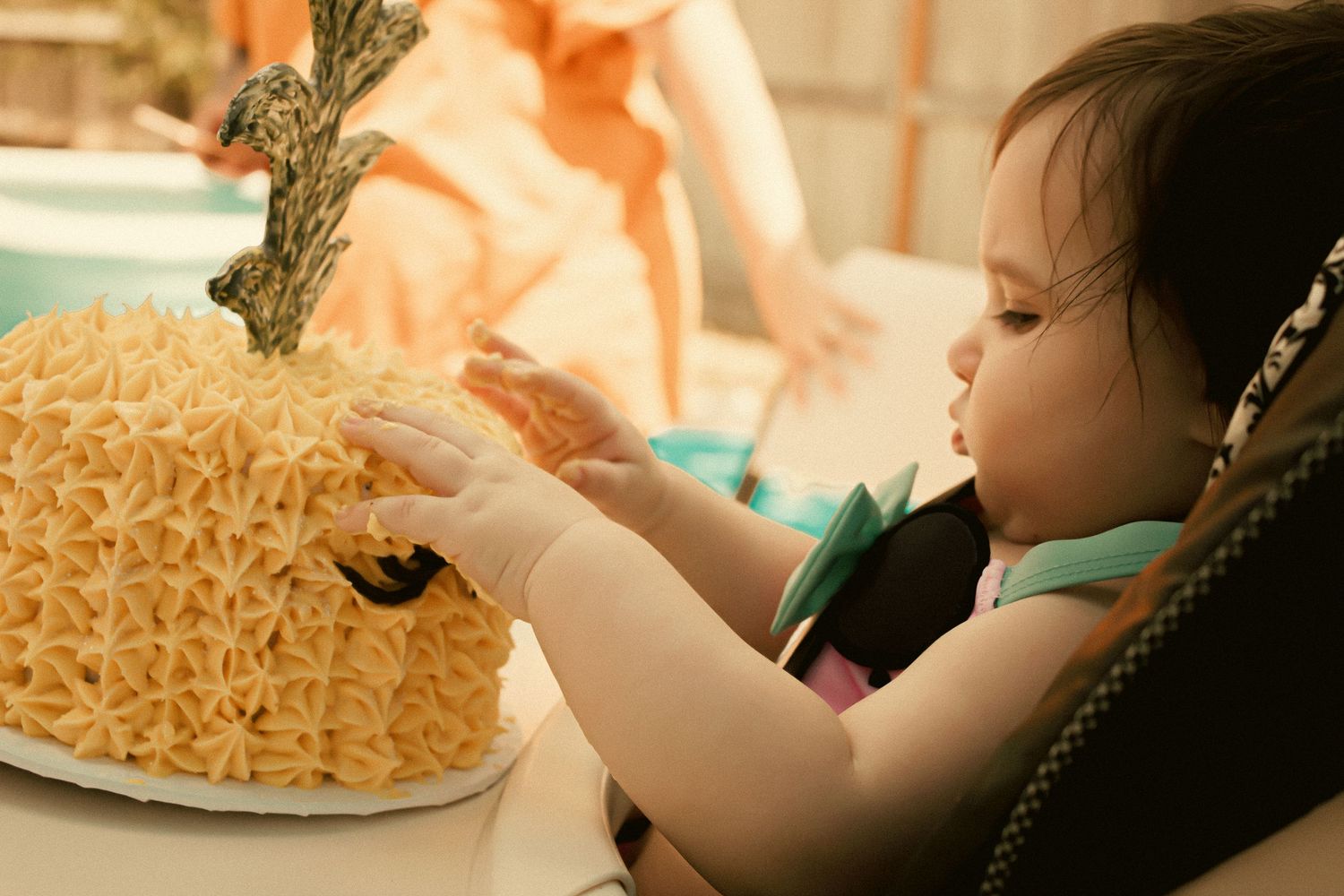 Baby touching a pineapple-shaped birthday cake while sitting in a high chair at a first birthday party.