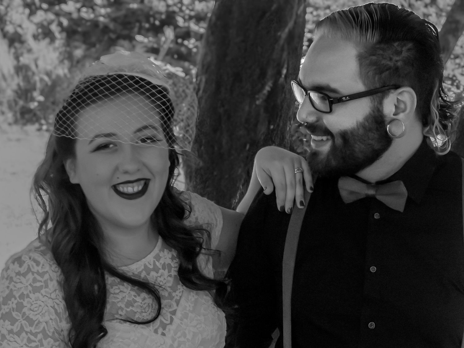 Black and white photo of a smiling couple, woman in lace dress with birdcage veil, man in bow tie and suspenders.