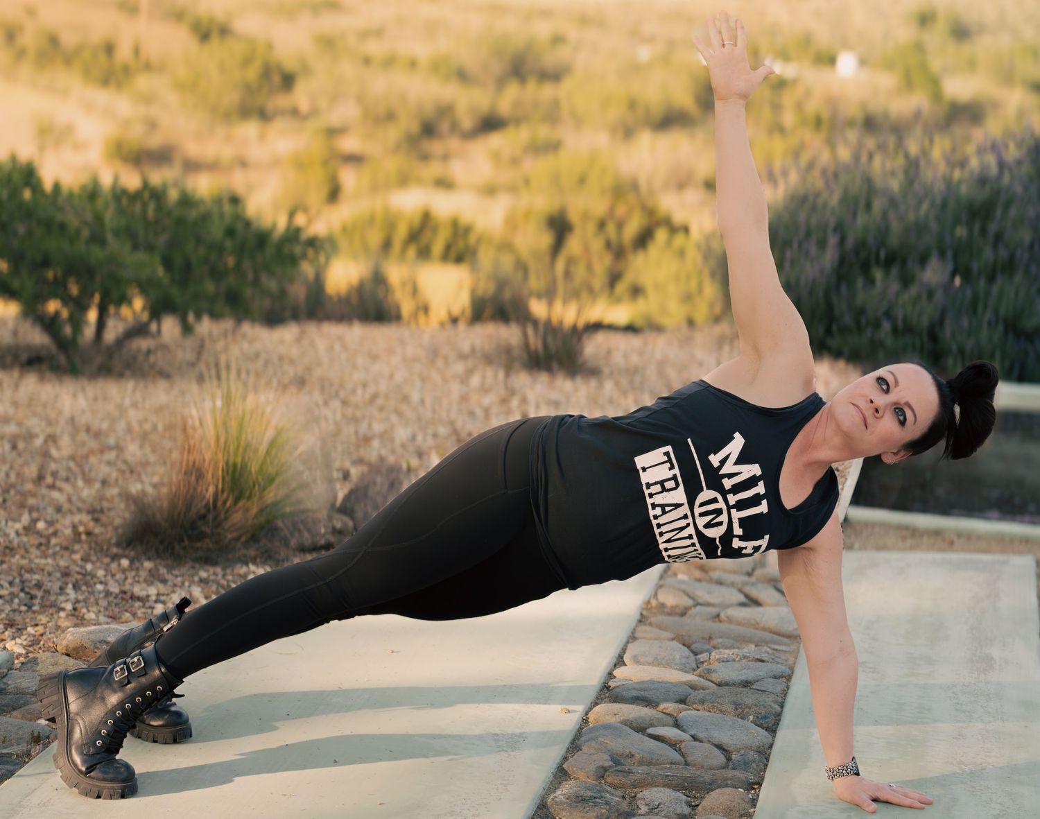 Woman performing a side plank yoga pose outdoors in black athletic wear, with desert landscape in background.