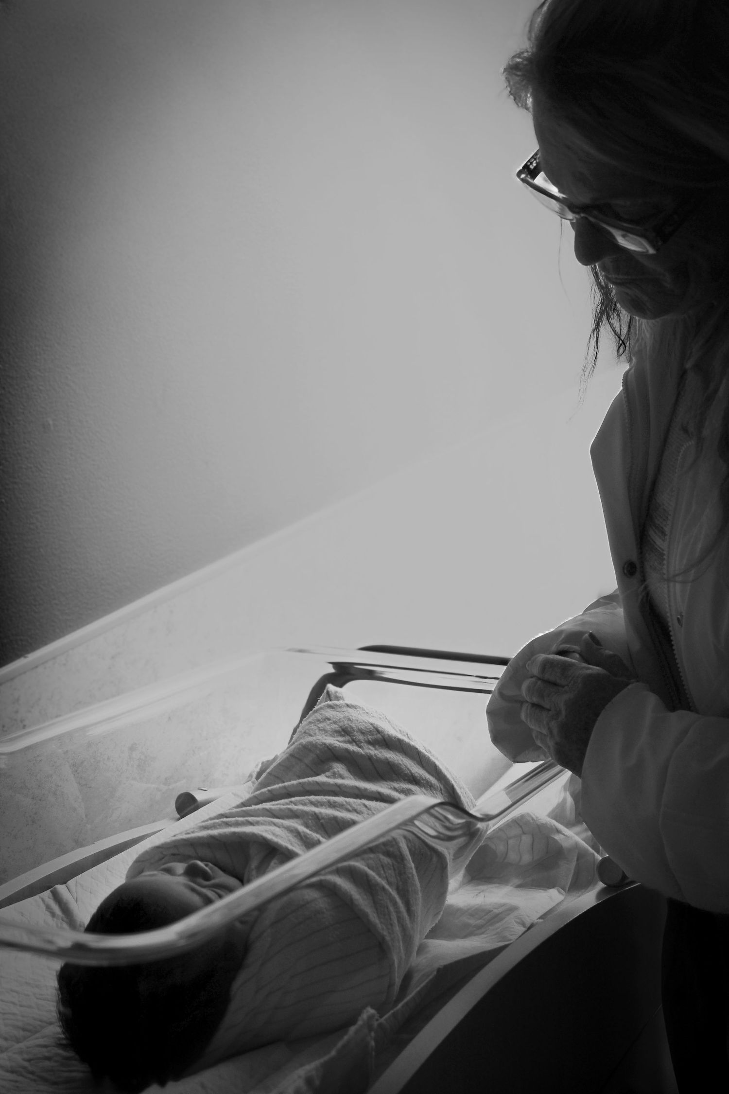 Black and white photo of nurse caring for swaddled newborn baby in hospital bassinet. fresh 48 hospital