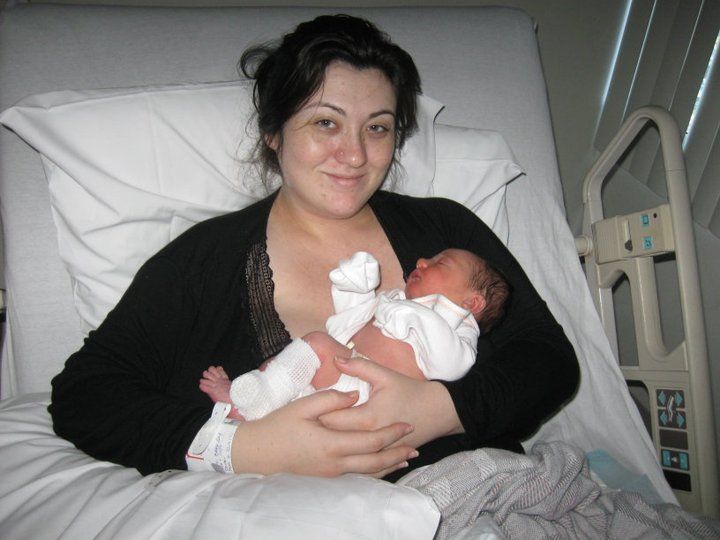 New mother holding her newborn baby in a hospital bed, dressed in a black cardigan after giving birth.