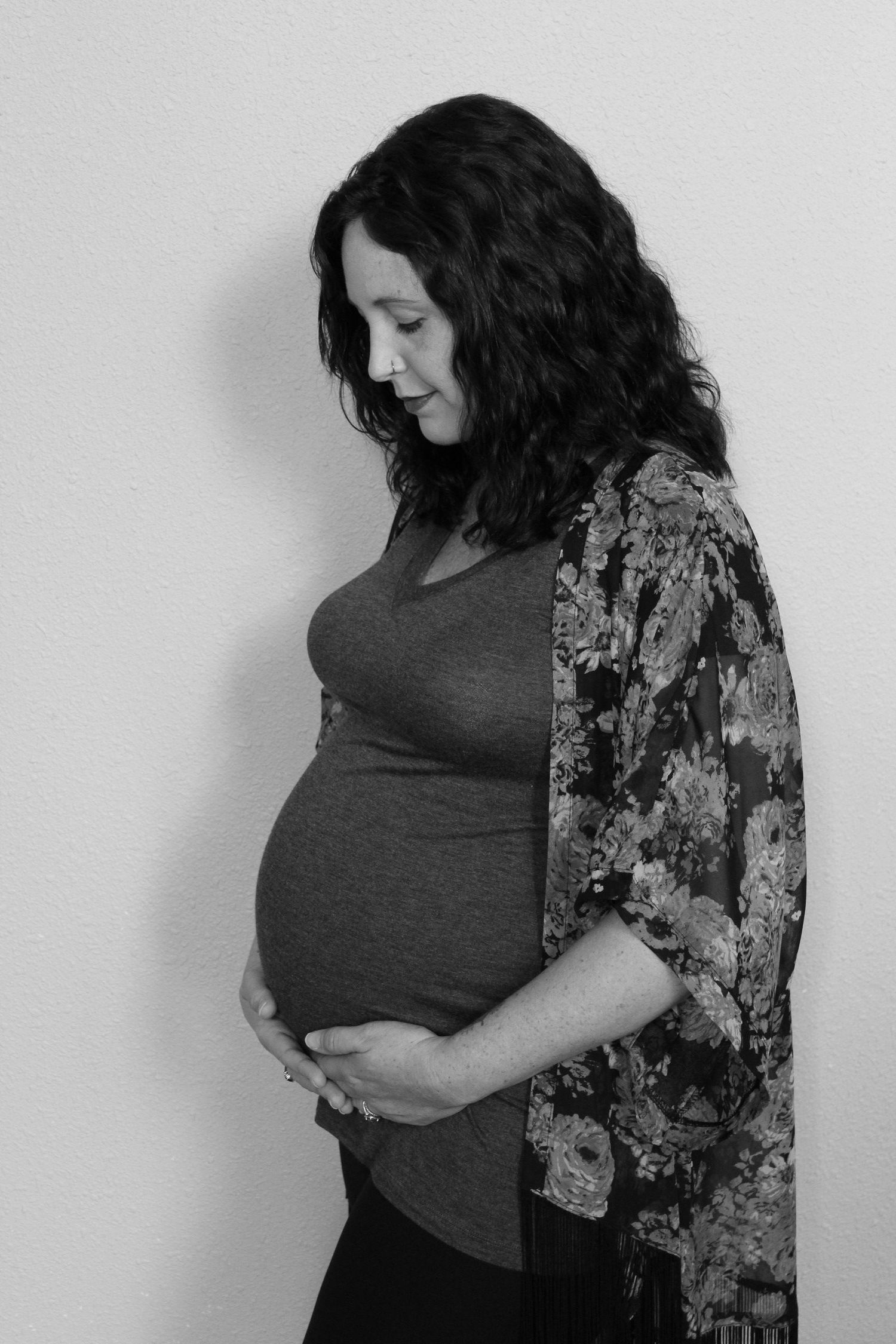 Black and white photo of a pregnant woman with curly dark hair cradling her baby bump while looking down tenderly.