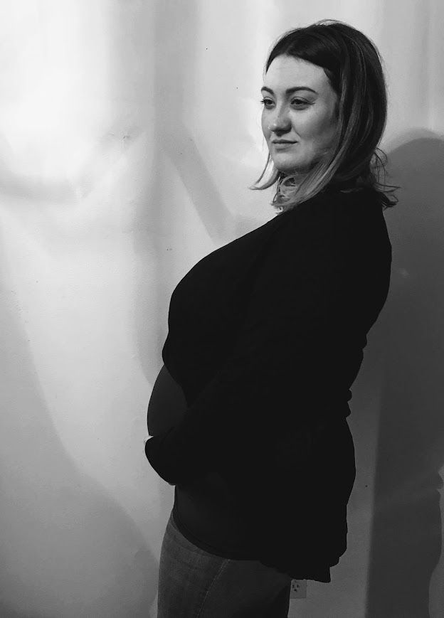 Black and white profile photo of a pregnant woman in a black sweater standing against a light background.