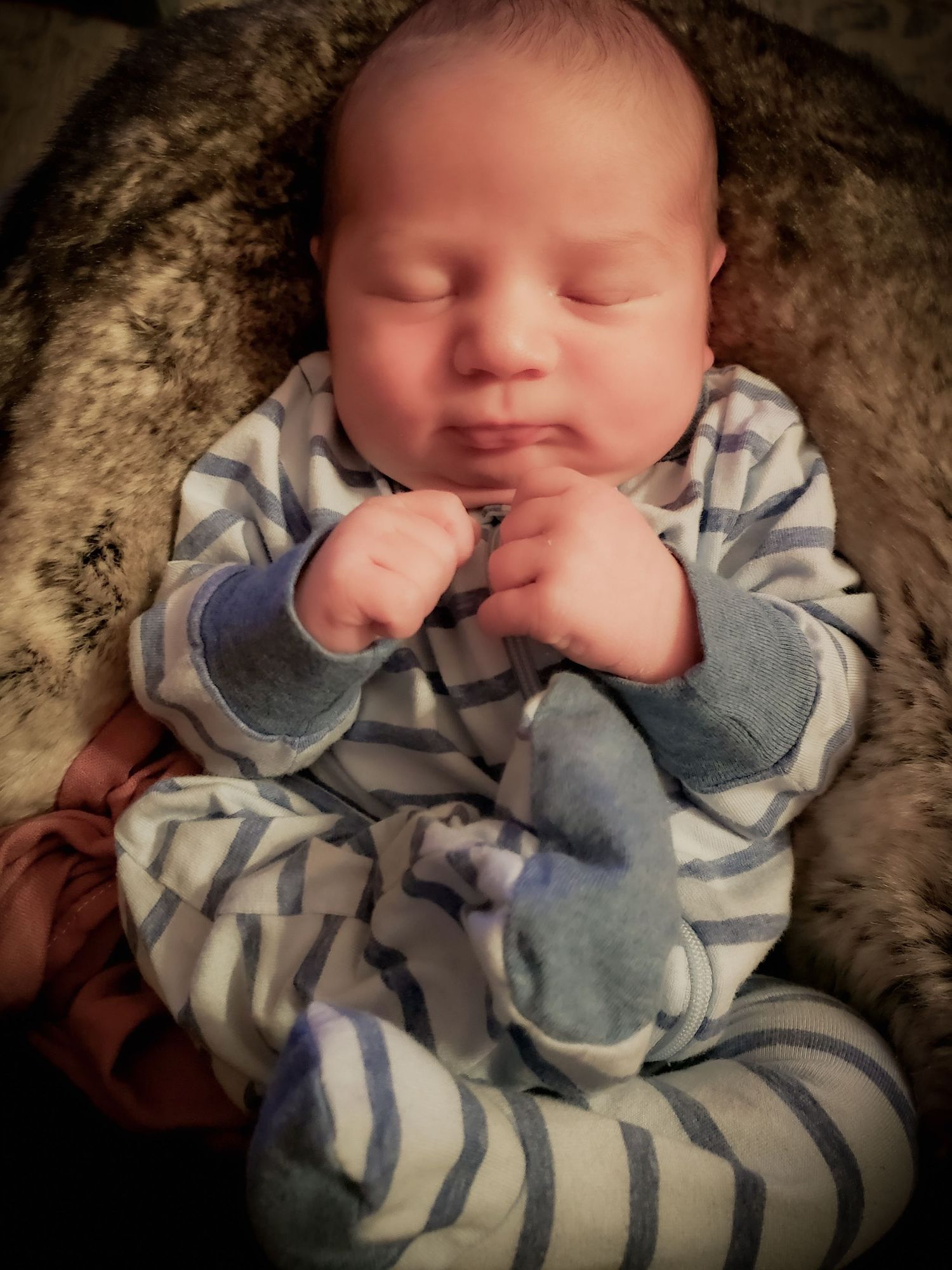 Newborn baby sleeping peacefully in striped onesie with mittens, nestled in a soft furry blanket.