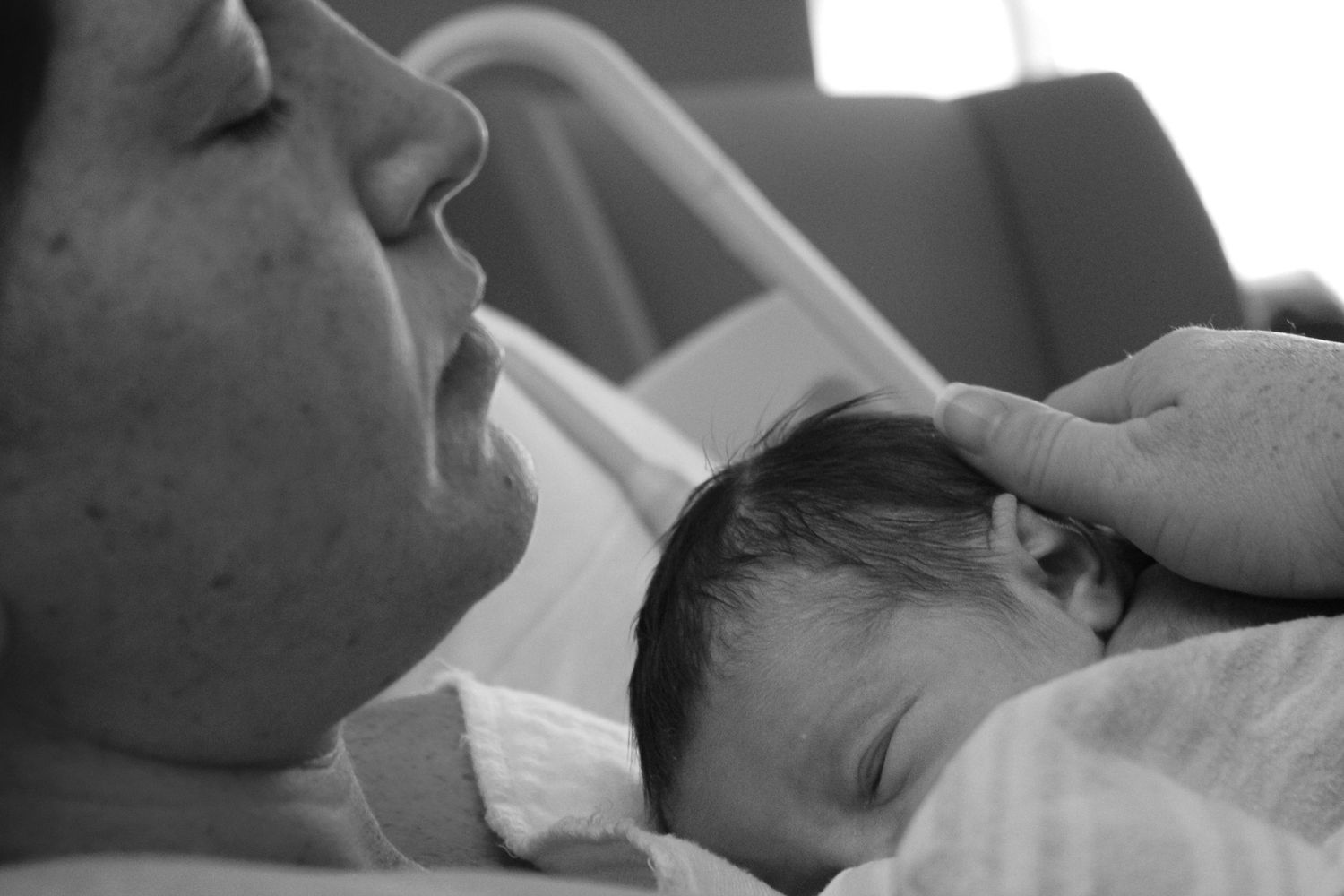 Black and white photo of a parent tenderly cradling a newborn baby in a hospital setting.