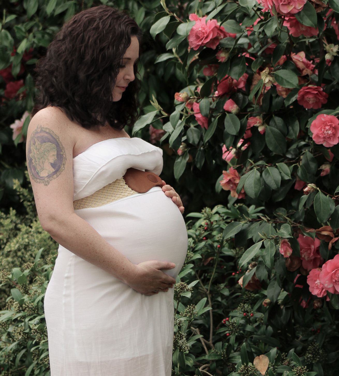 Maternity photo outside with pregnant mother in white strapless dress holding baby bump near  pink camellia at eve and Elm Albany, Oregon