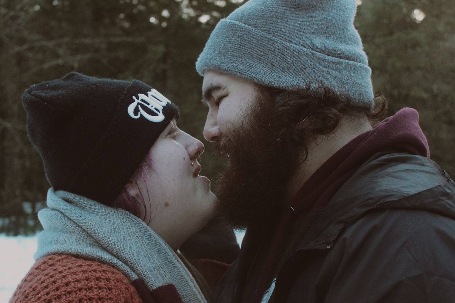 Couple in winter beanies sharing a romantic kiss outdoors in a snowy forest setting at mt. hood oregon
