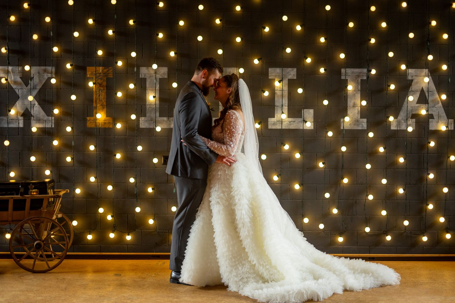 Wedding couple poses against backdrop of twinkling string lights creating magical atmosphere.