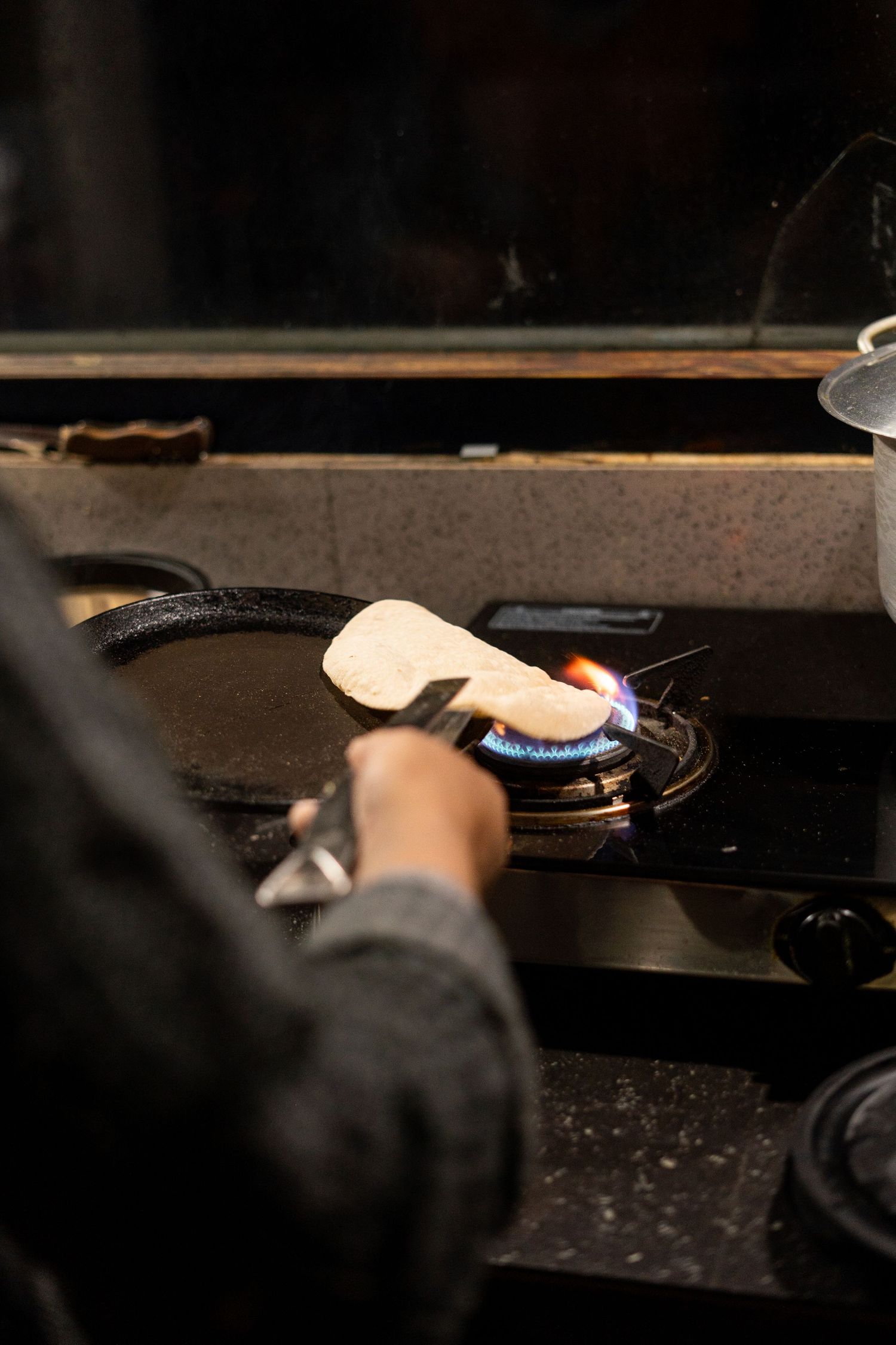 Close-up of a hand lighting a gas stove burner in a dark kitchen setting.